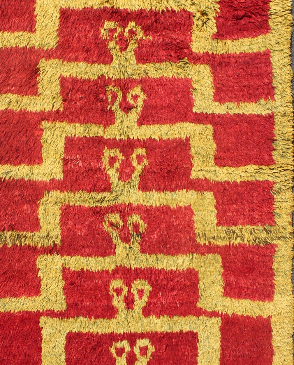 Made with fine wool and high pile, this vintage Tulu from mid-20th century Turkey boasts an interconnected Mid-Century Modern pattern. The multi-tiered pattern consists of greenish-gold outlines set on a red field. The contrast of color adds a