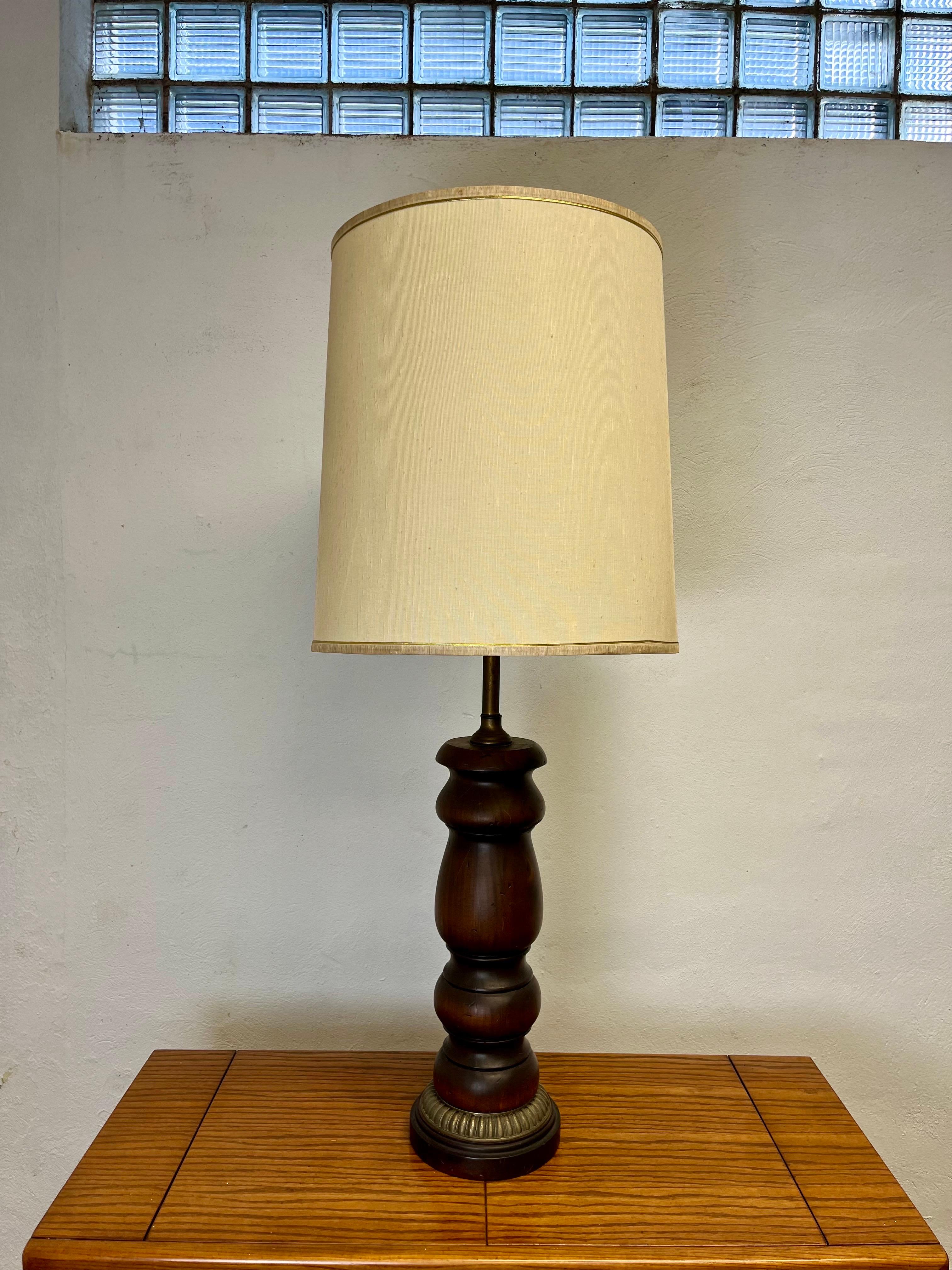 Lampada in legno splendidamente tornita. Forma classica per un fascino ampio con una patina meravigliosa. Il corpo di forma maschile è compensato da un anello di ottone intorno alla base. L'ombra d'epoca completa il tutto. 
Misure del corpo