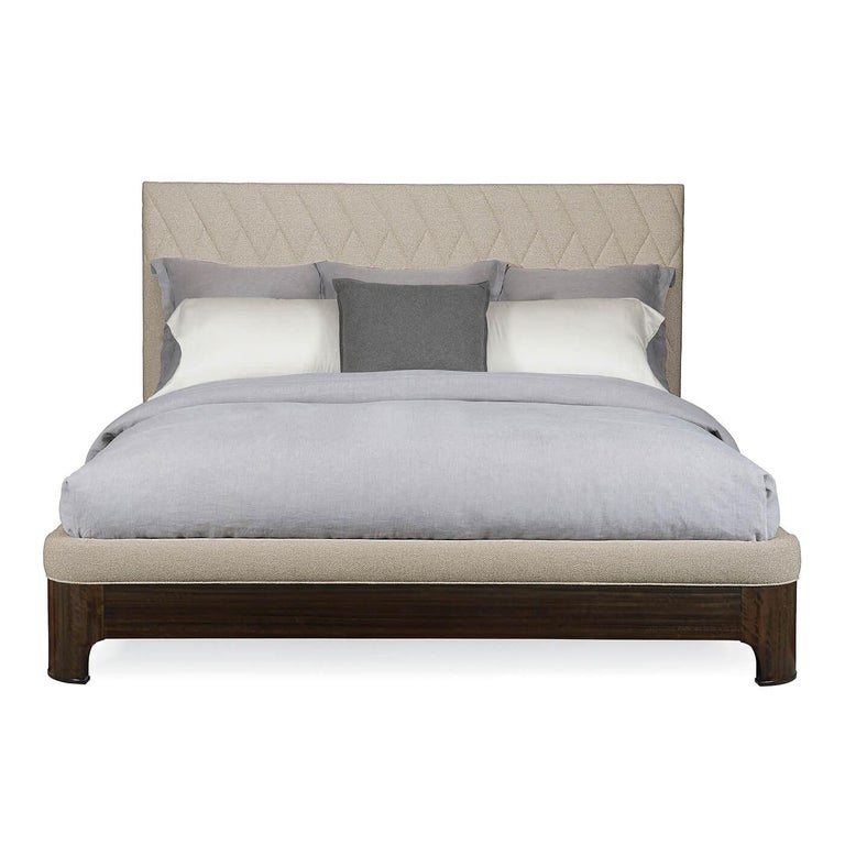 A Mid-Century Modern style tweed upholstered king bed. The quilted upholstered headboard has a herringbone pattern. An exposed frame of fumed figured eucalyptus, finished in Aged Bourbon, trims the headboard, footboard, and rails that are also