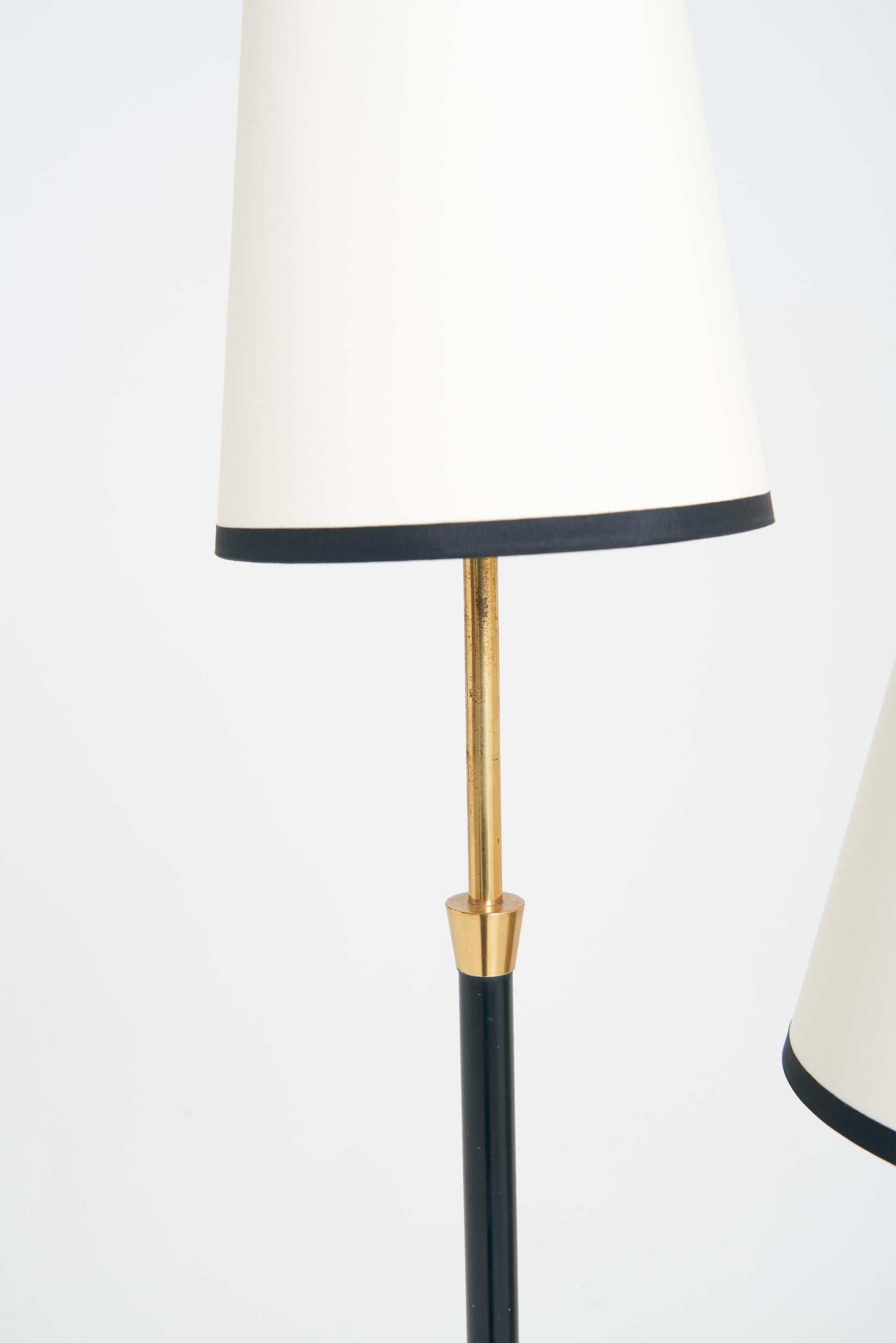 A brass and black enamel two-arm floor lamp
Sweden, mid 20th Century
With the shades: 161 cm high by 34 cm diameter 
Lamp base only: 146 cm high by 27 cm diameter