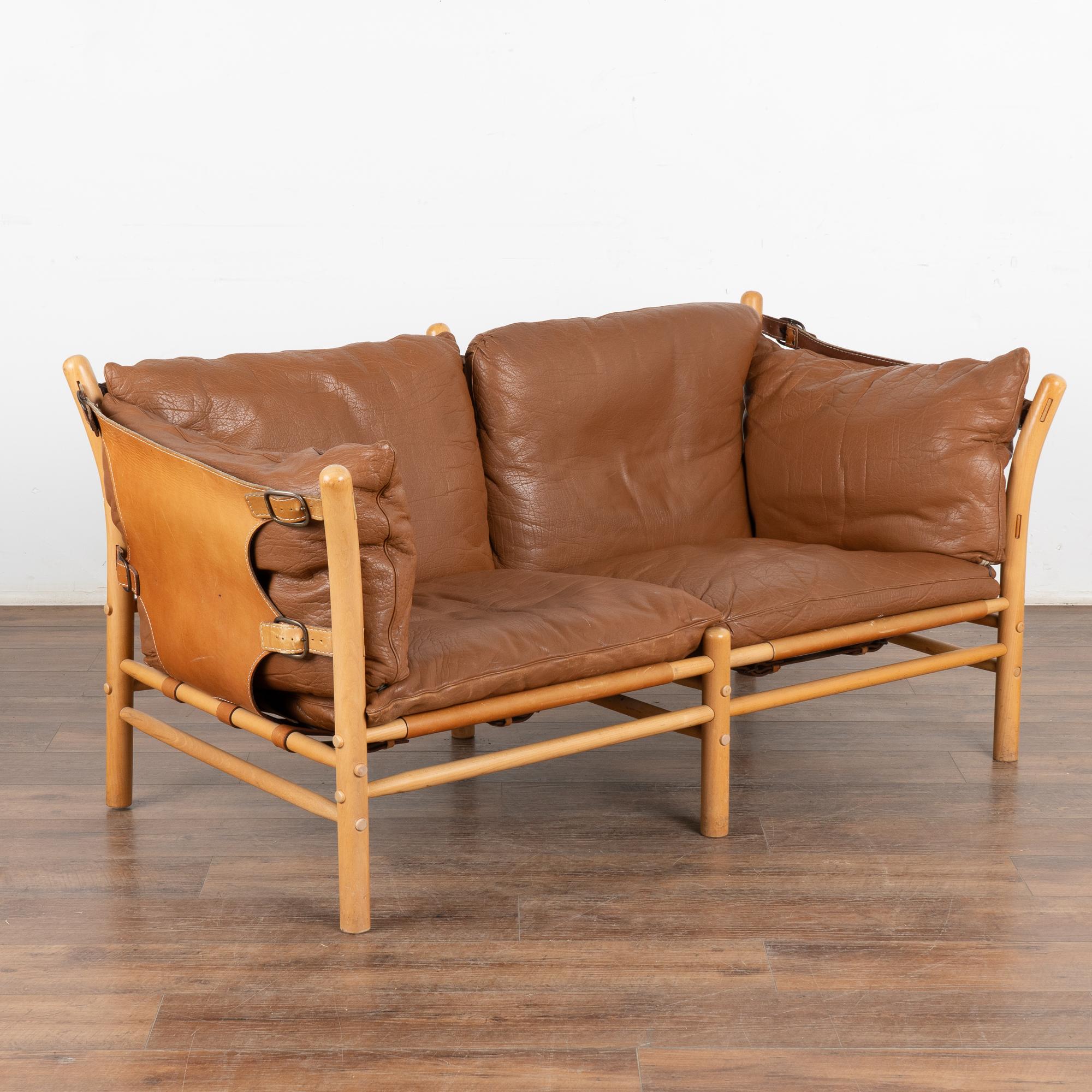 Mid-Century Modern two-person sofa designed by Arne Norell. Leather sling sides and back, brass hardware, loose cushions with zippered covers. The Ilona model was inspired by safari furniture and manufactured by Aneby Møbler (makers mark