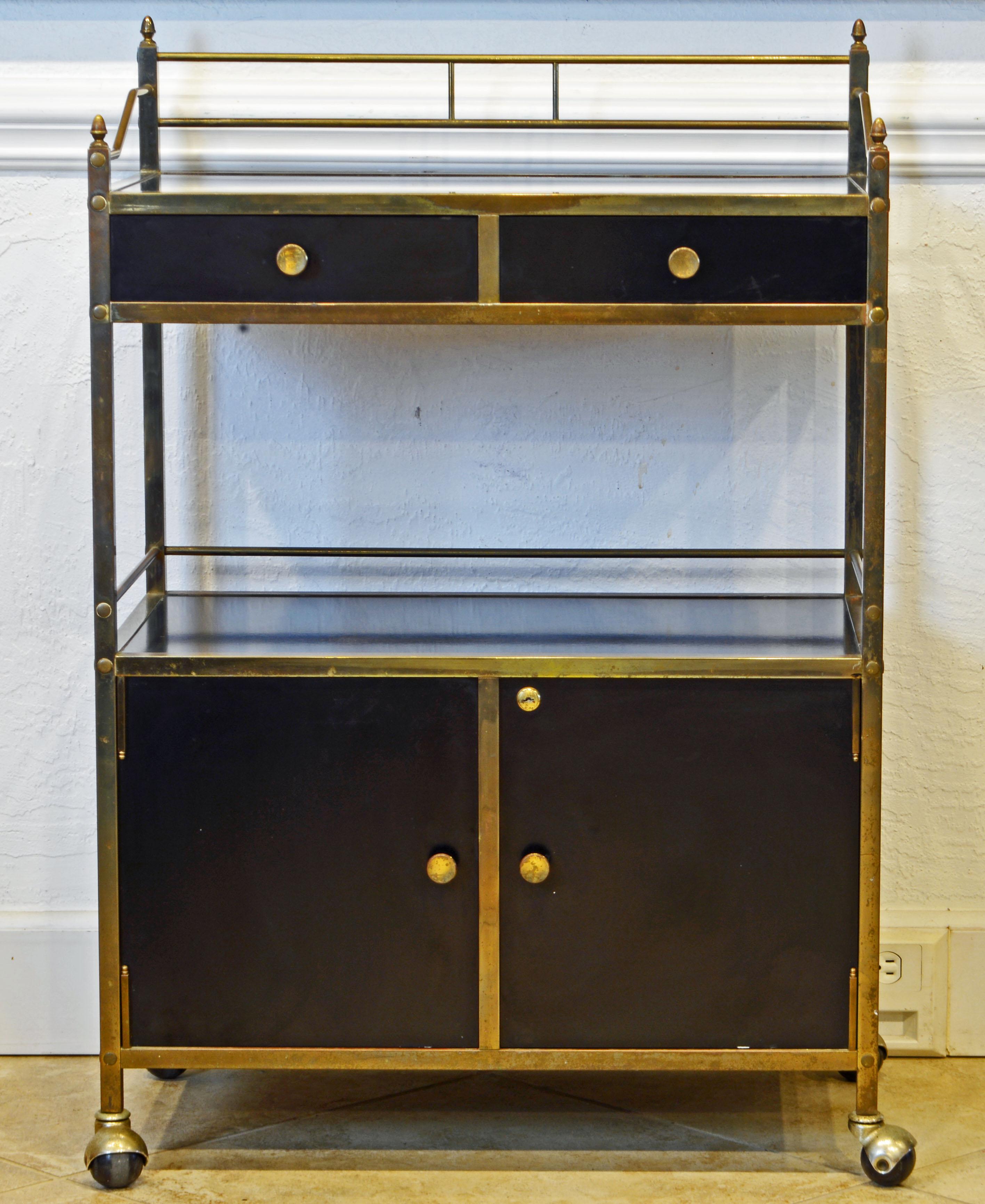This well designed bar cart or server dating to the 1960-1970 features frames of solid brass and surfaces of black lacquer or laminate in an almost Bauhaus like style. The upper rail is topped by acorn shaped finials. The lower section features a