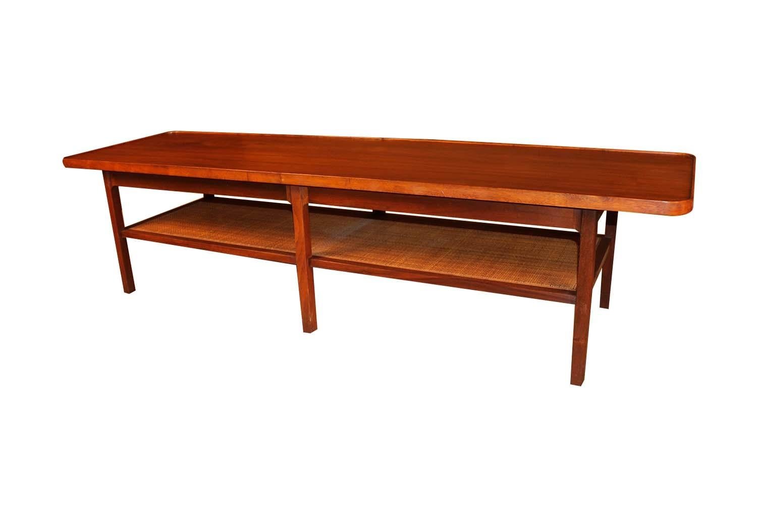 A beautiful Mid Century two tier coffee table. The perfect length to pair with an extra long sofa. Features a rectangular top with a raised walnut edge-banding that runs the length of the table’s upper ridge, enhancing the sleek profile. A unique,