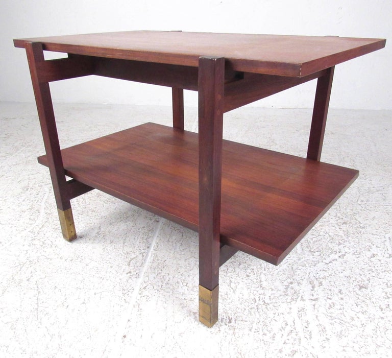 This vintage modern end table features solid walnut construction, brass sabot feet, and stylish two-tier construction. Unique end table is perfect for bedside storage, lamp table, or living room sofa table. Please confirm item location (NY or NJ).