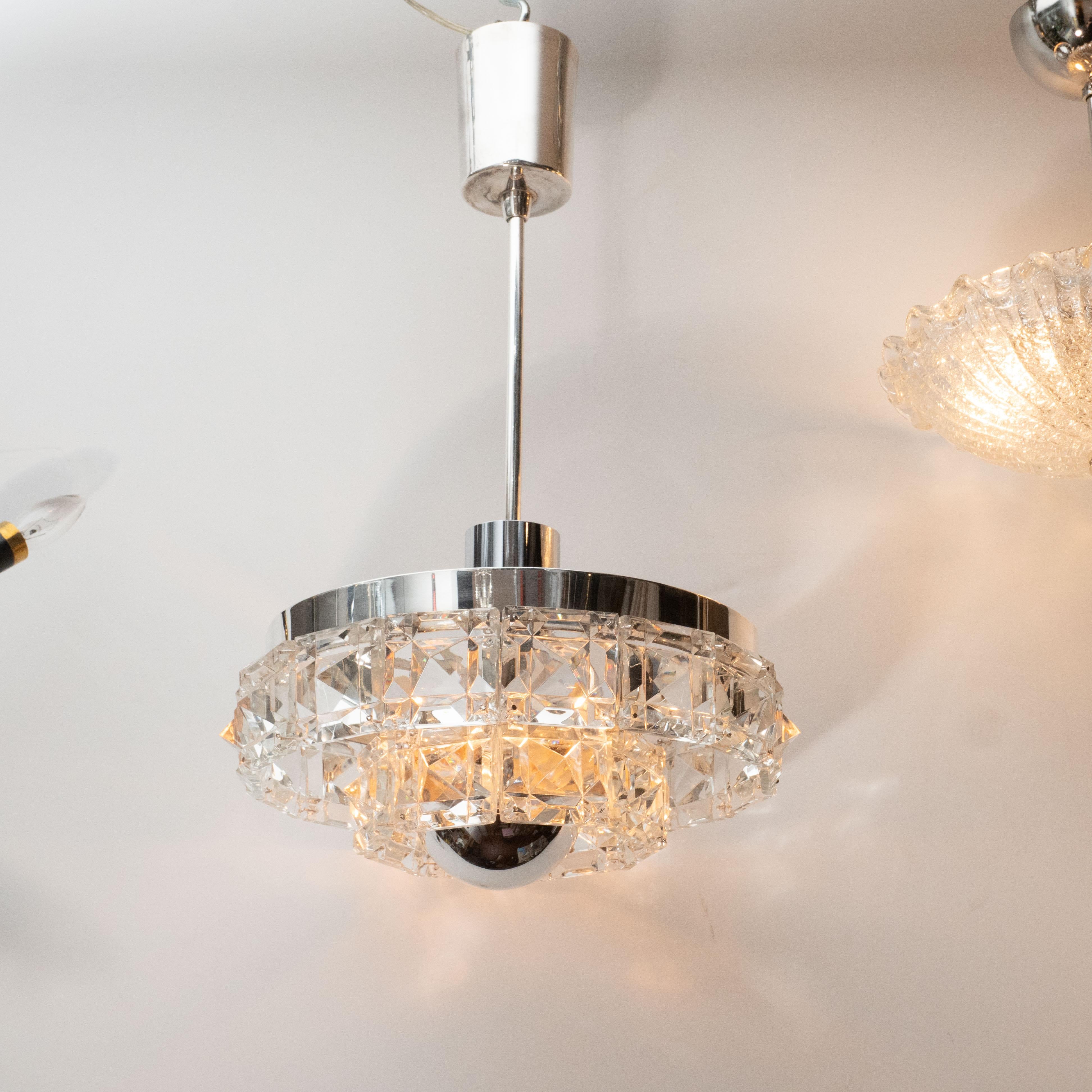 This elegant Mid-Century Modern chandelier was realized by the esteemed maker Kinkeldey in Austria circa 1960. It features two circular tiers of faceted crystal (resembling oversized cut diamonds) connected to a polished chrome frame. The fixture