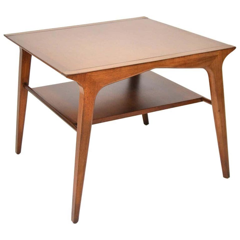 A rare vintage Mid-Century Modern end table designed by John Van Koert for Drexel's Profile collection, model K73, dating from 1956. The walnut and pecan two-tiered occasional table features a square top, a magazine shelf, and the designer's