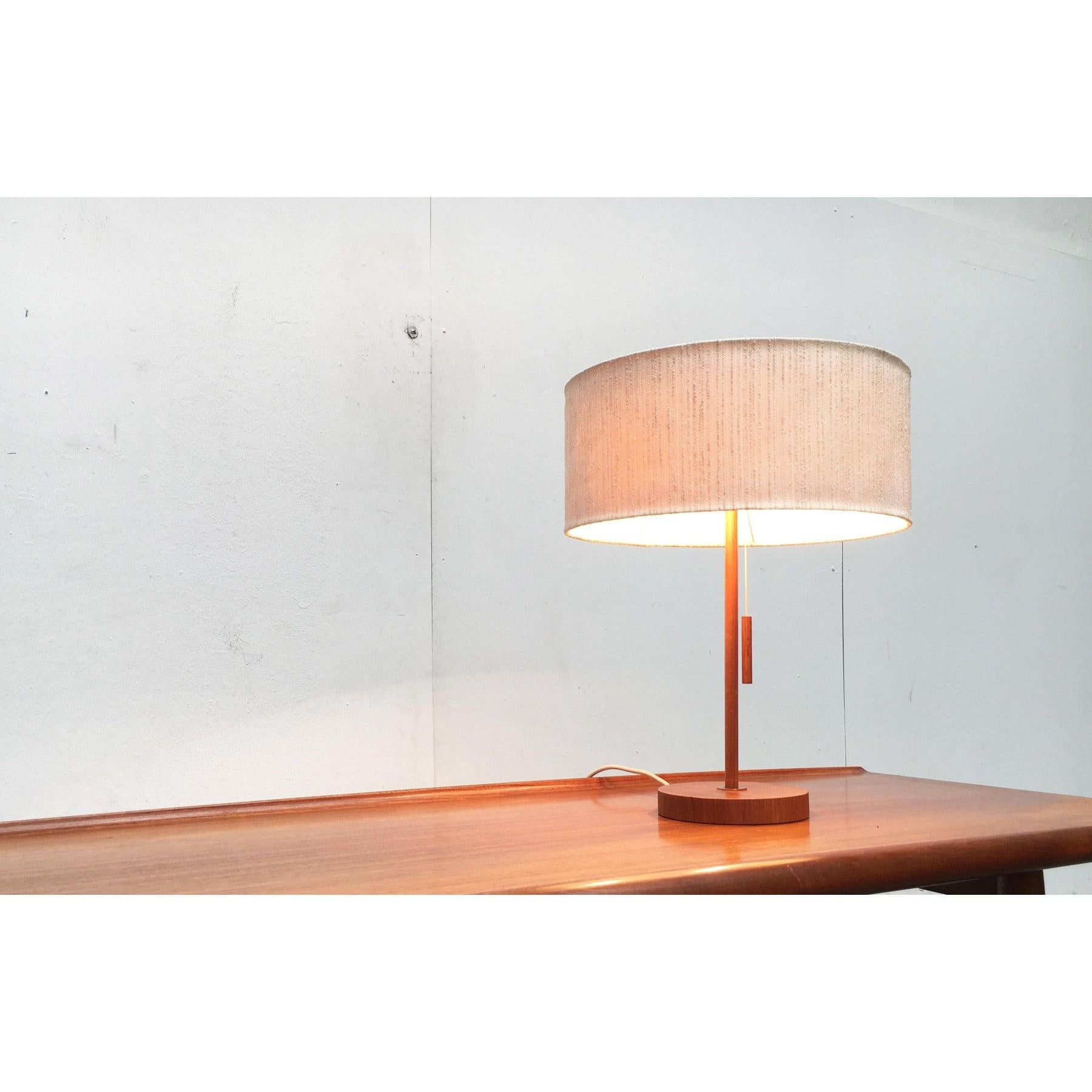 Mid-Century teak table lamp from the Swiss manufacturer Temde.

Simple design language in high quality materiality. The textile shade has a simple drum shape. On the top is inlaid a griffed diffuser disc made of acrylic. The teak shaft merges into a