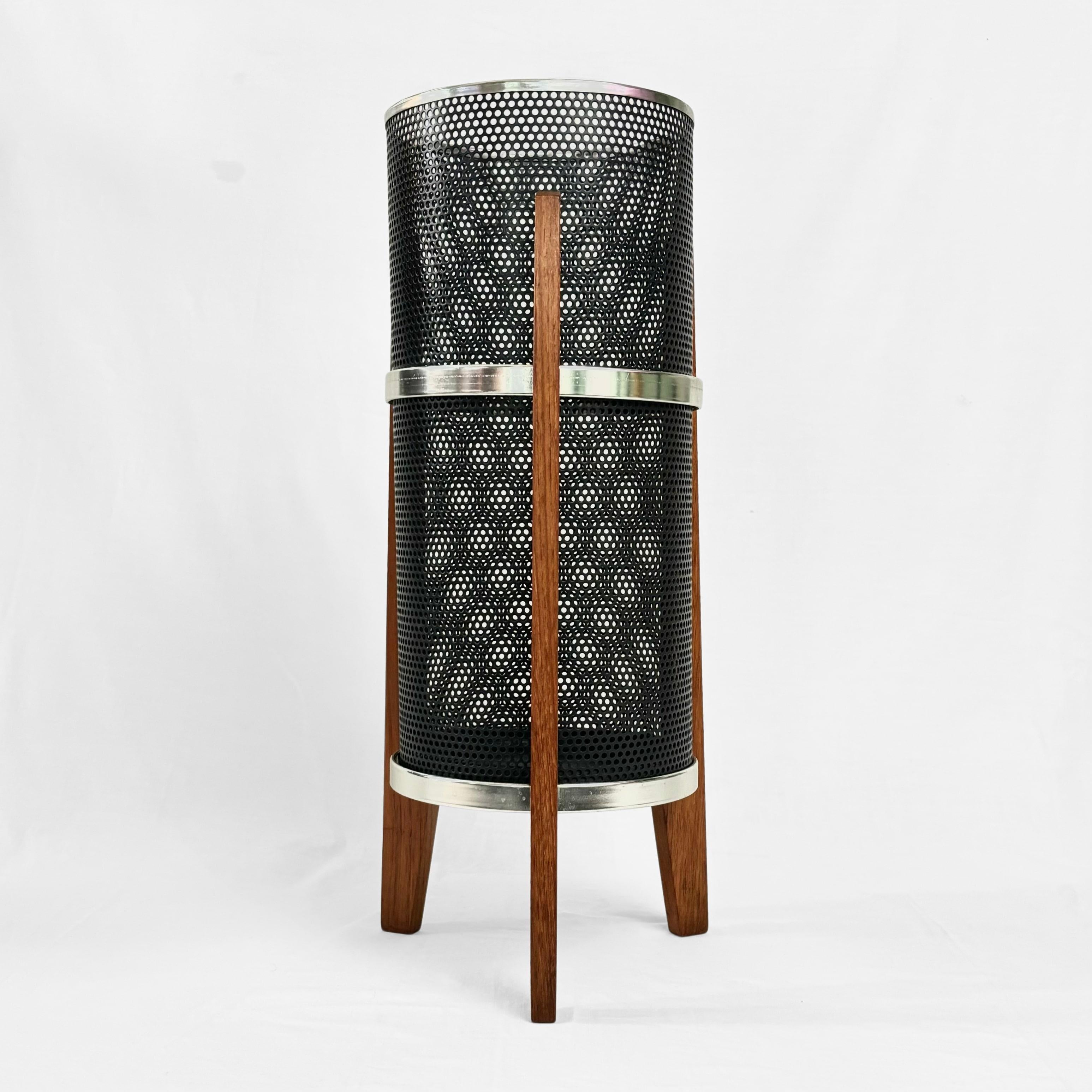 Porte-parapluie ou corbeille à papier moderniste, fabriqué en métal perforé noir avec une base en fonte verte et un rebord chromé au sommet. Il repose sur une base tripode en teck maintenue par des anneaux en métal chromé. Produit par un fabricant
