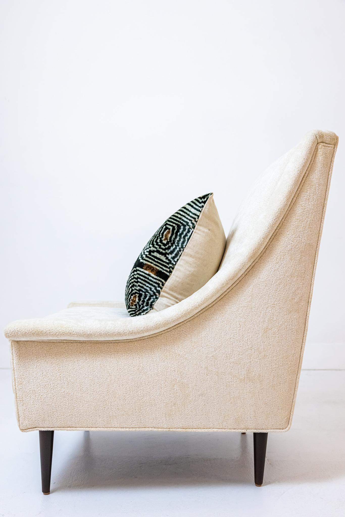 This is a stylish and classic mid century arm chair that has been newly upholstered in a beautiful soft cream chenille fabric. Four dark wooden legs support the chair. This would be amazing as a lounge chair in a bedroom or a side chair in any
