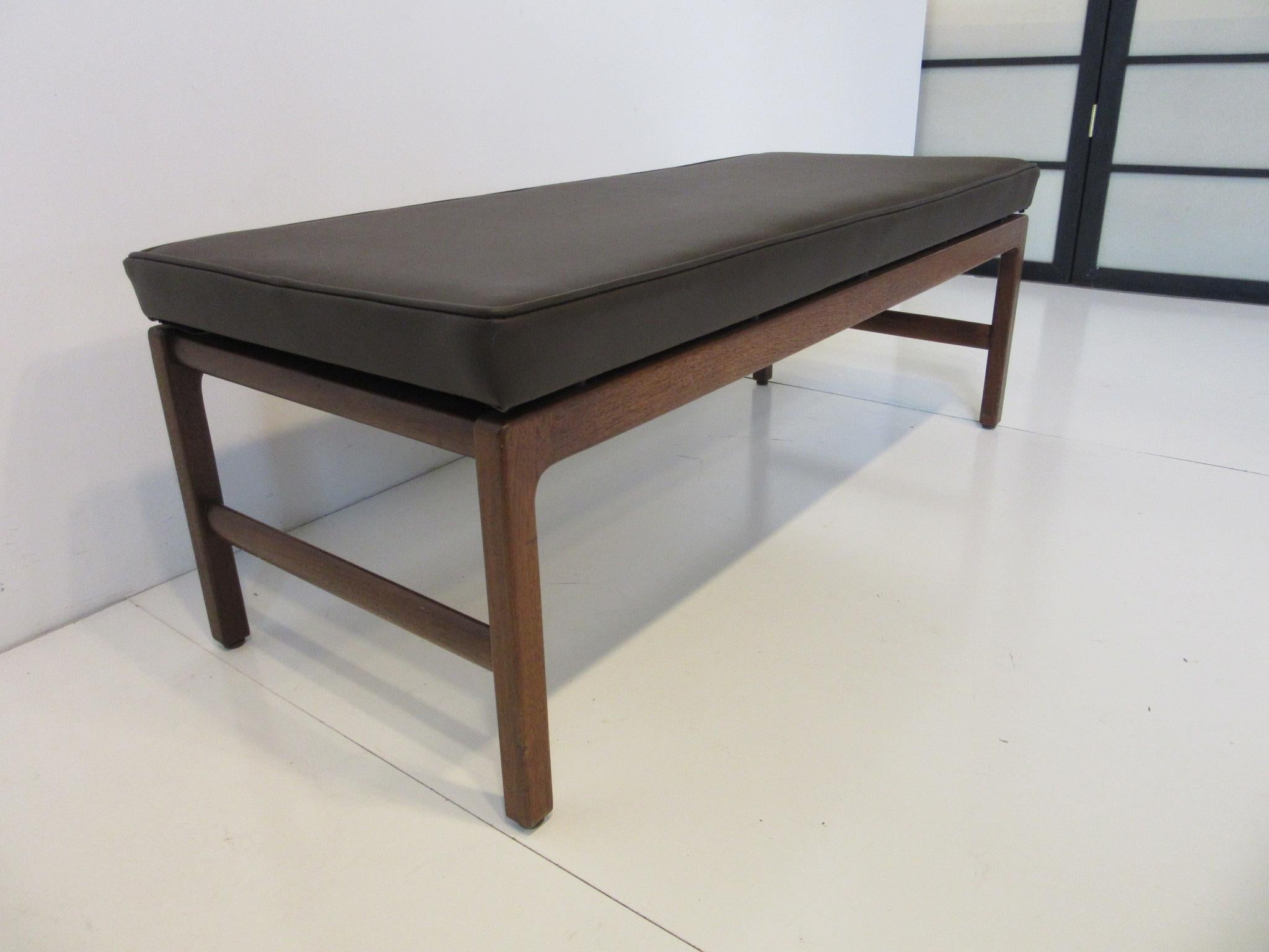 A walnut based upholstered bench with floating seat in dark brown leatherette manufactured in the manner of Jens Risom.