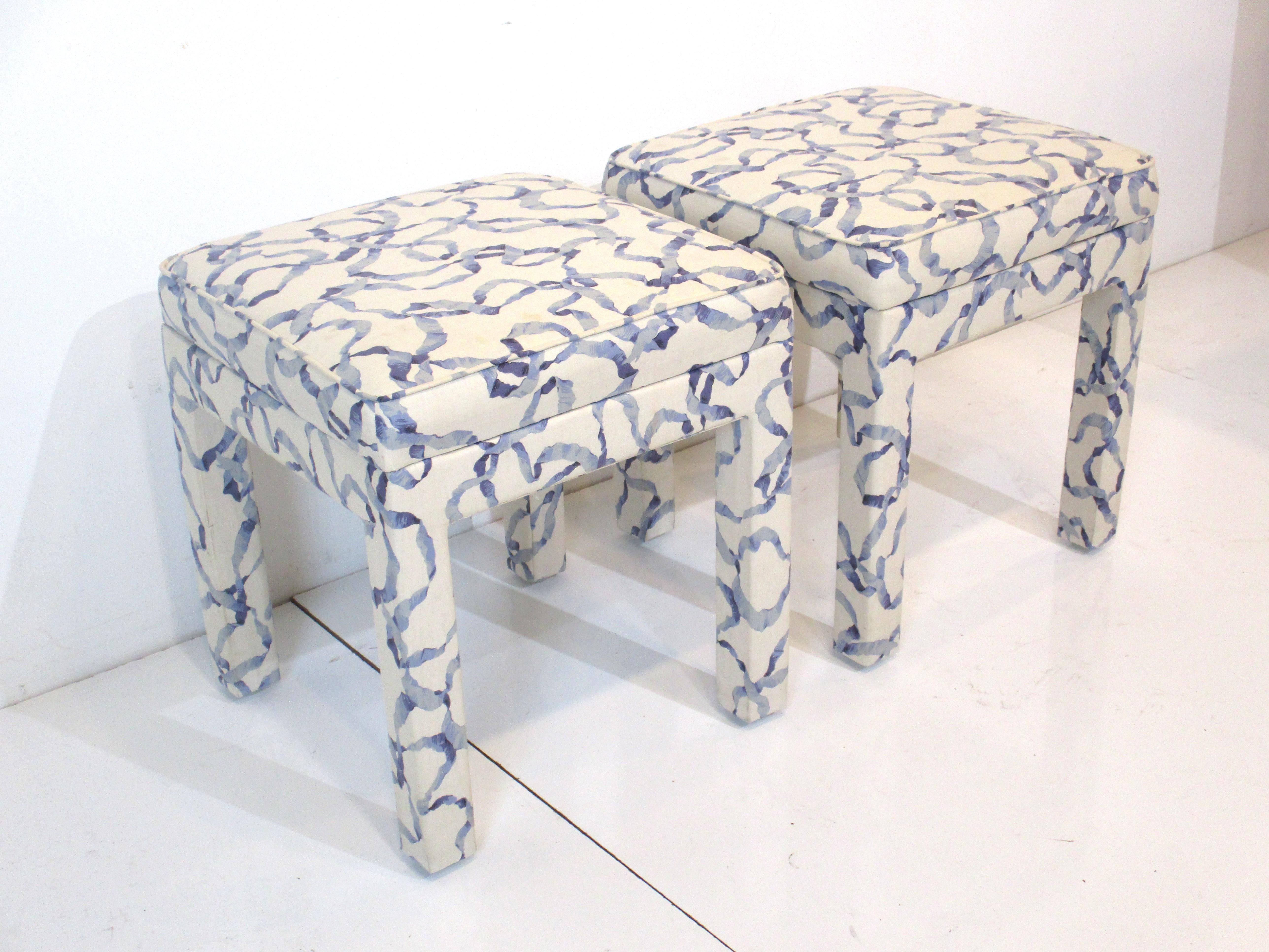 Un par de taburetes tapizados de buen tamaño en tela azul y crema, perfectos como asiento extra o para guardar debajo de una consola . Fabricado a la manera de la empresa Henredon Furniture.