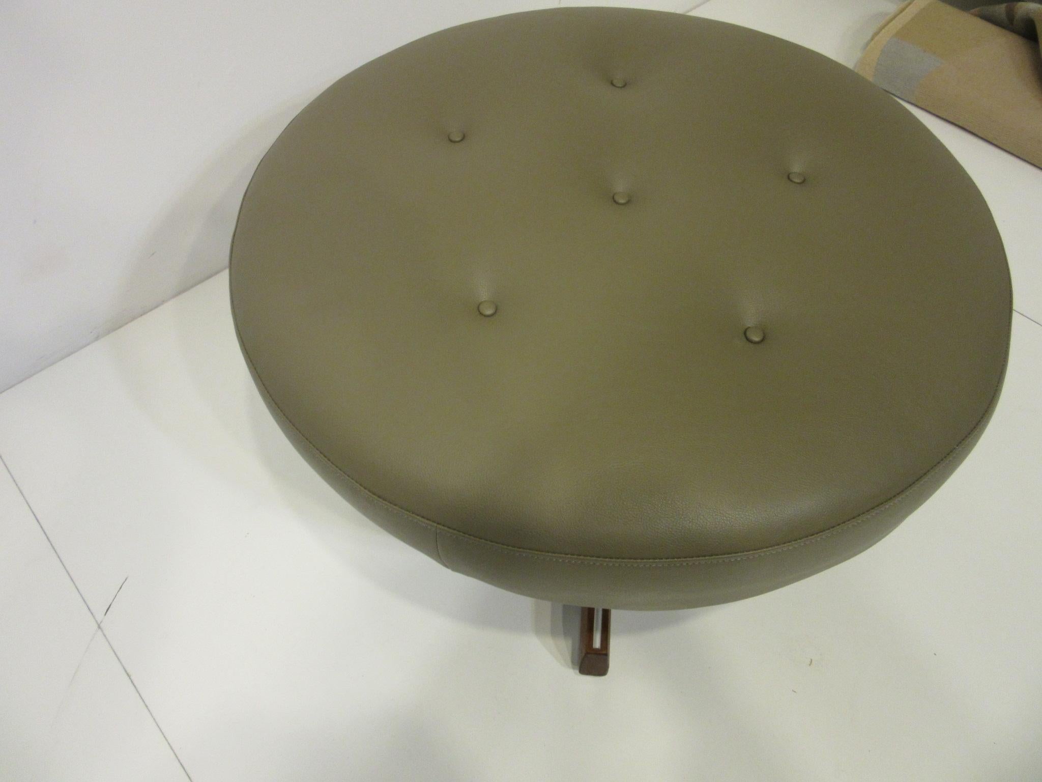 A midcentury swiveling ottoman with walnut base and brushed metal detail strips to the legs, there are adjustable foot pads to each. The button tufted (gray / green) very similar to Sherwood Williams SW -7046 toned cushion can be used alone as extra