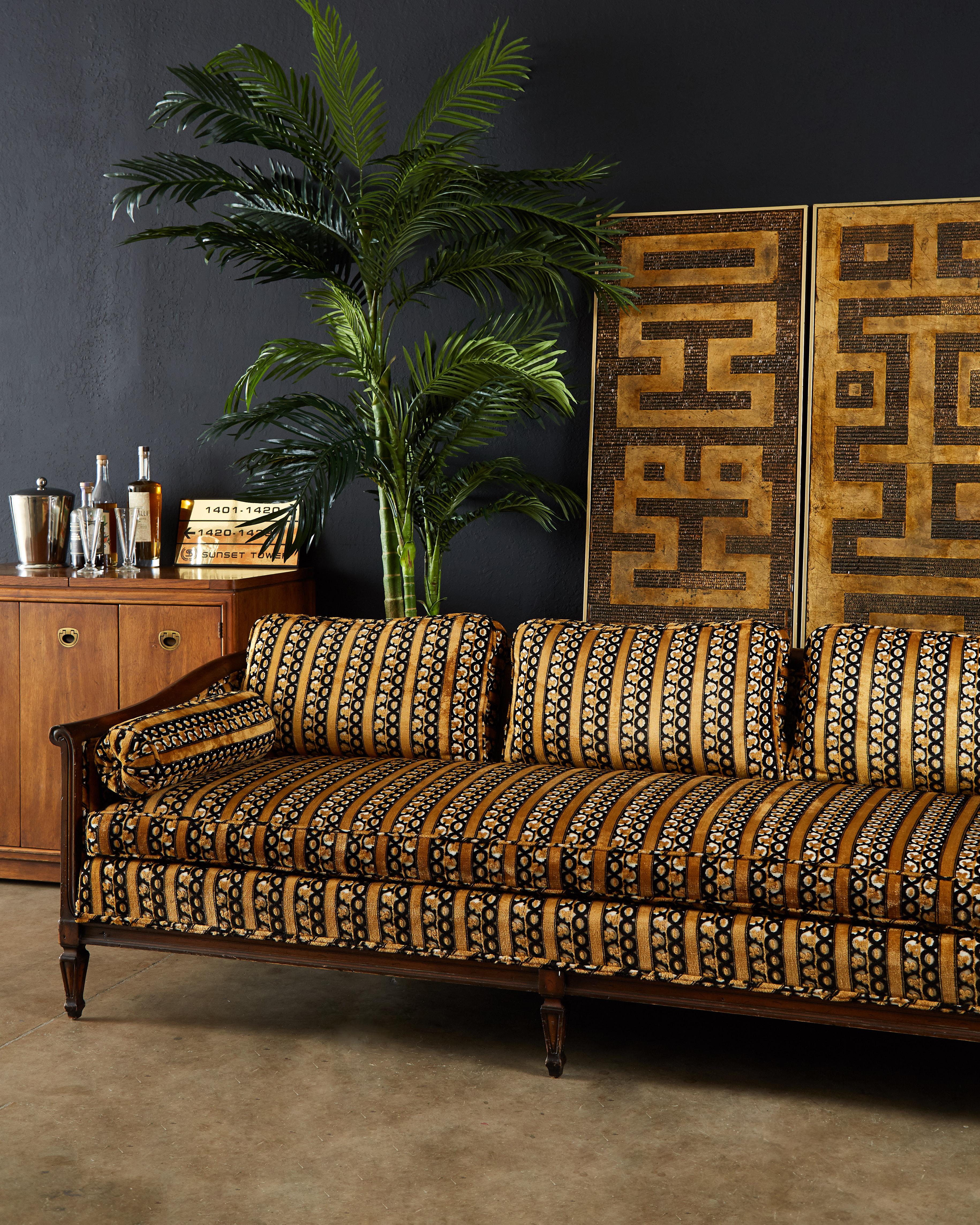Chic midcentury walnut three-seat sofa featuring a Versace-esque upholstery by Dunbar. The walnut frame was constructed with a low profile case design having graceful sloping arms and back. The walnut has a beautiful lightly distressed finish and