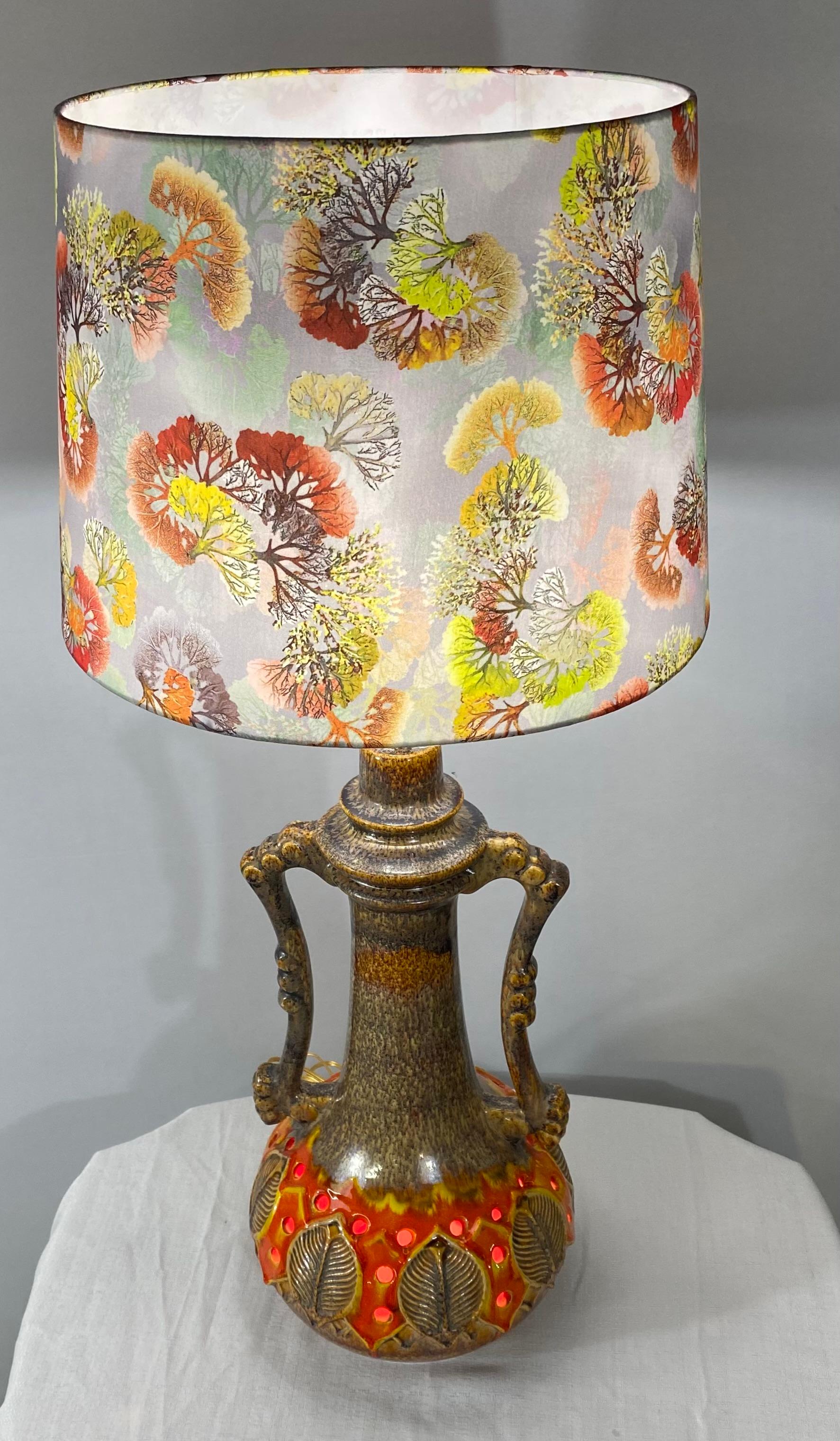 A lovely and one of a kind mid-century jar or urn converted table lamp. The finely glazed ceramic lamp features two nicely carved handles and beautiful leaves design around the lamp body. The earthy orange and brown colors tone of the lamp are