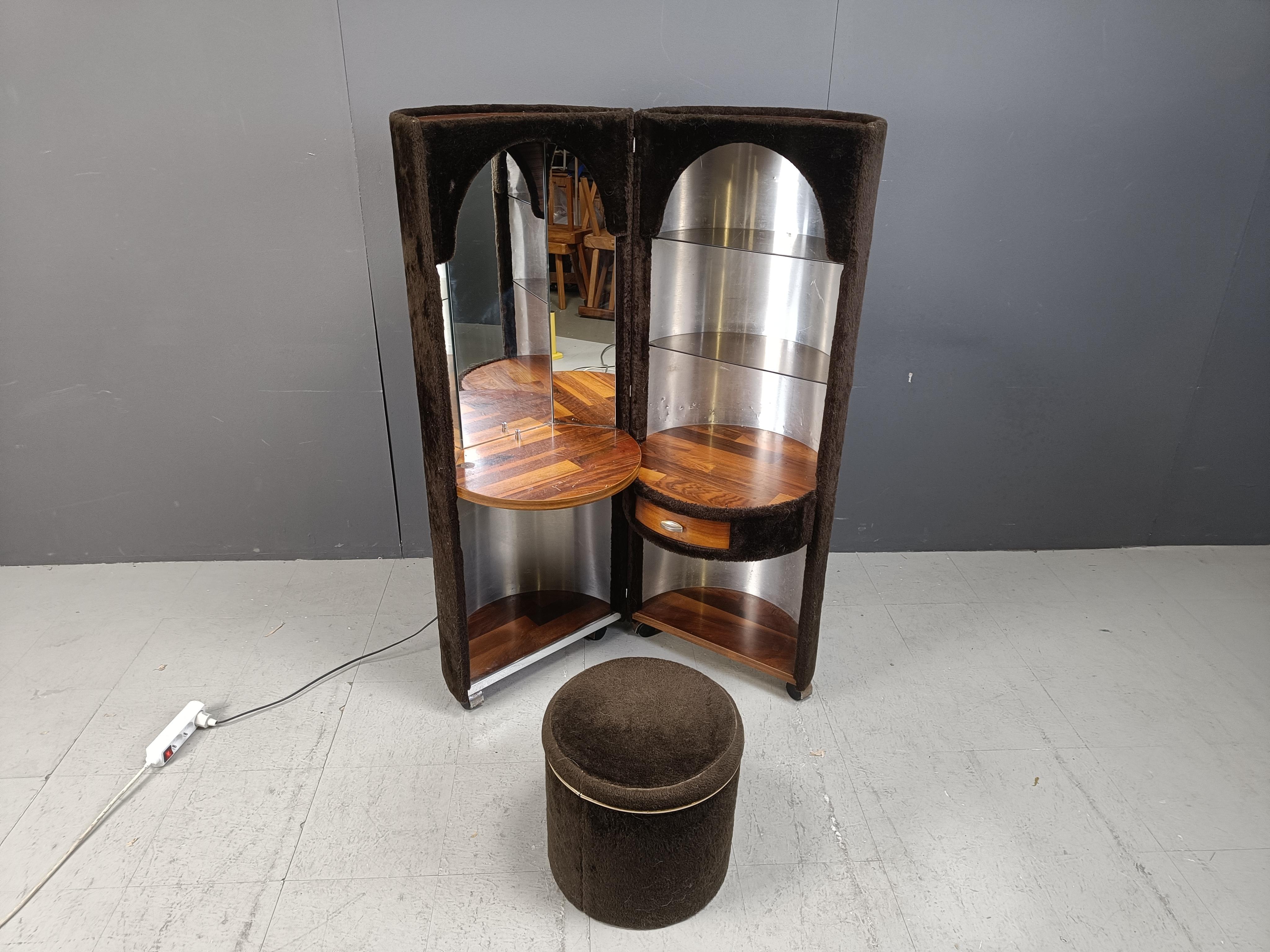 Very 'seventies' make up cabinet on wheels with integrated mirrors, lights, a drawer and glass shelves, complete with stool which is mostly missing.

This item has great seventies vibes.

Covered in brown artificial fur.

Nice and high quality wood