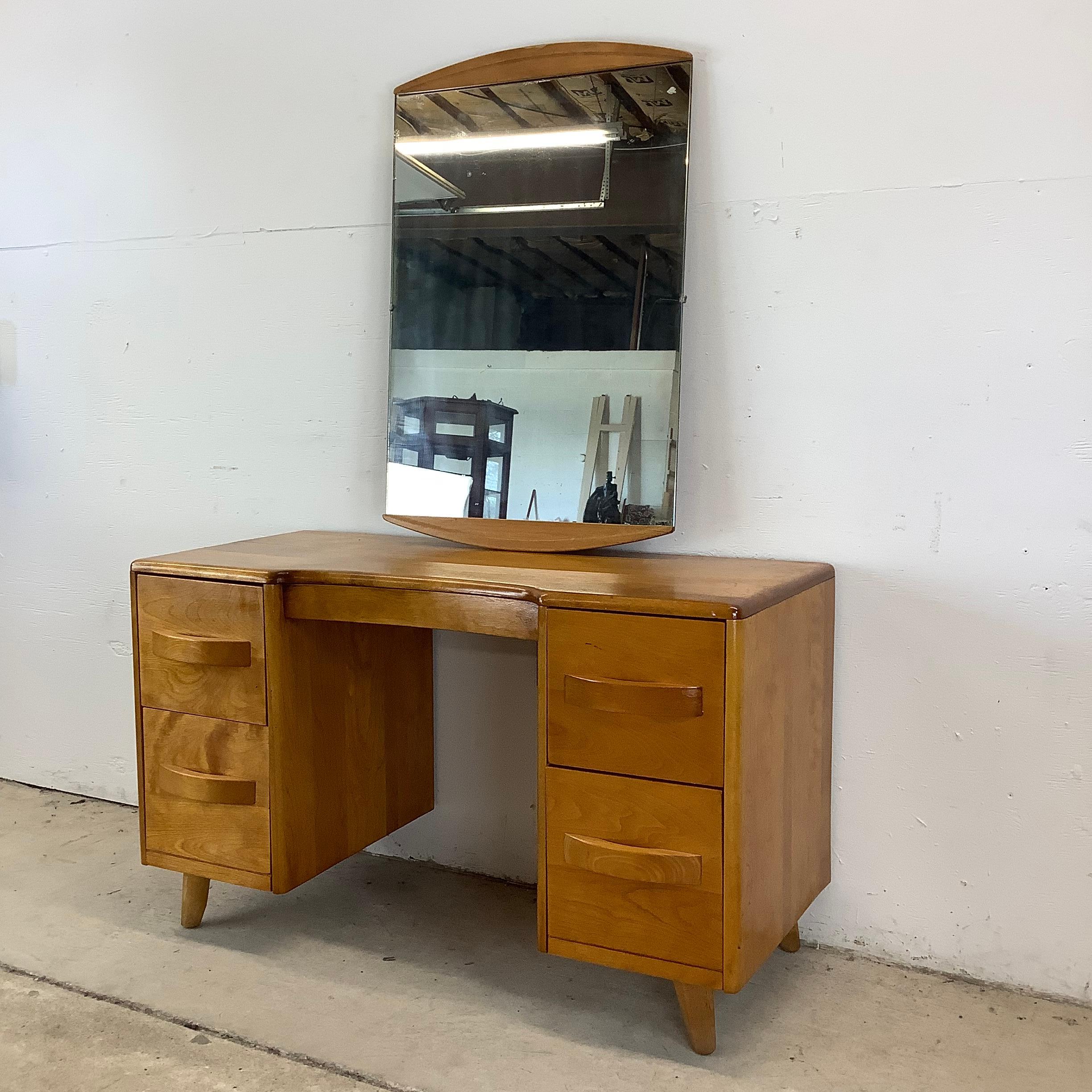 Élevez votre espace avec ce meuble-lavabo et son miroir en érable du milieu du siècle par Heywood Wakefield, un exemple stupéfiant d'art fonctionnel. Avec son design épuré et sa luxueuse finition en bois doré, cette pièce est l'incarnation du style