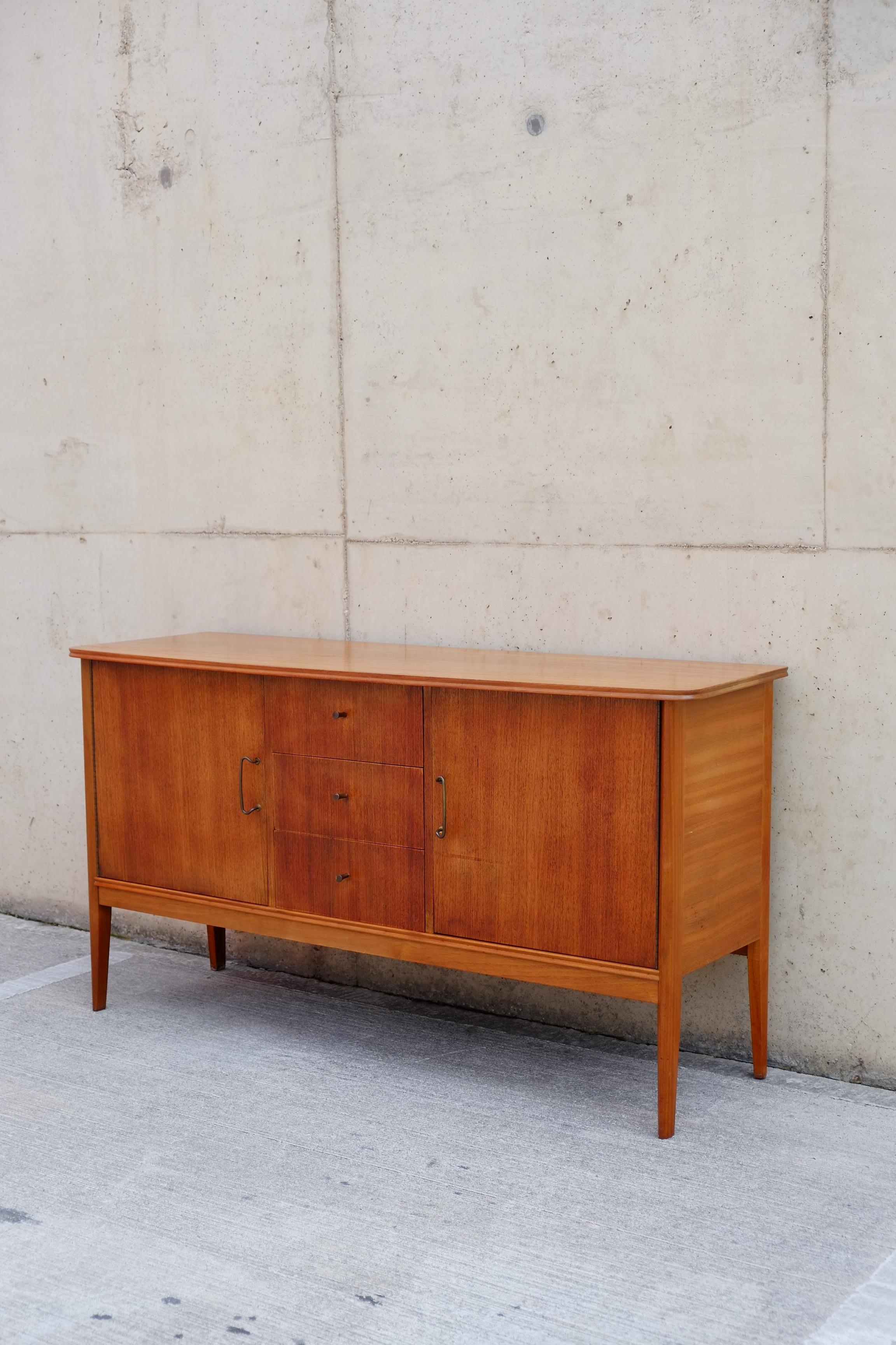 A beautiful 1960s sideboard by quality cabinet maker Vanson. This sideboard was handmade in England with beautiful solid sapele and teak woods. The sideboard has two cupboards and three central drawers which are finished with beautifully shaped,
