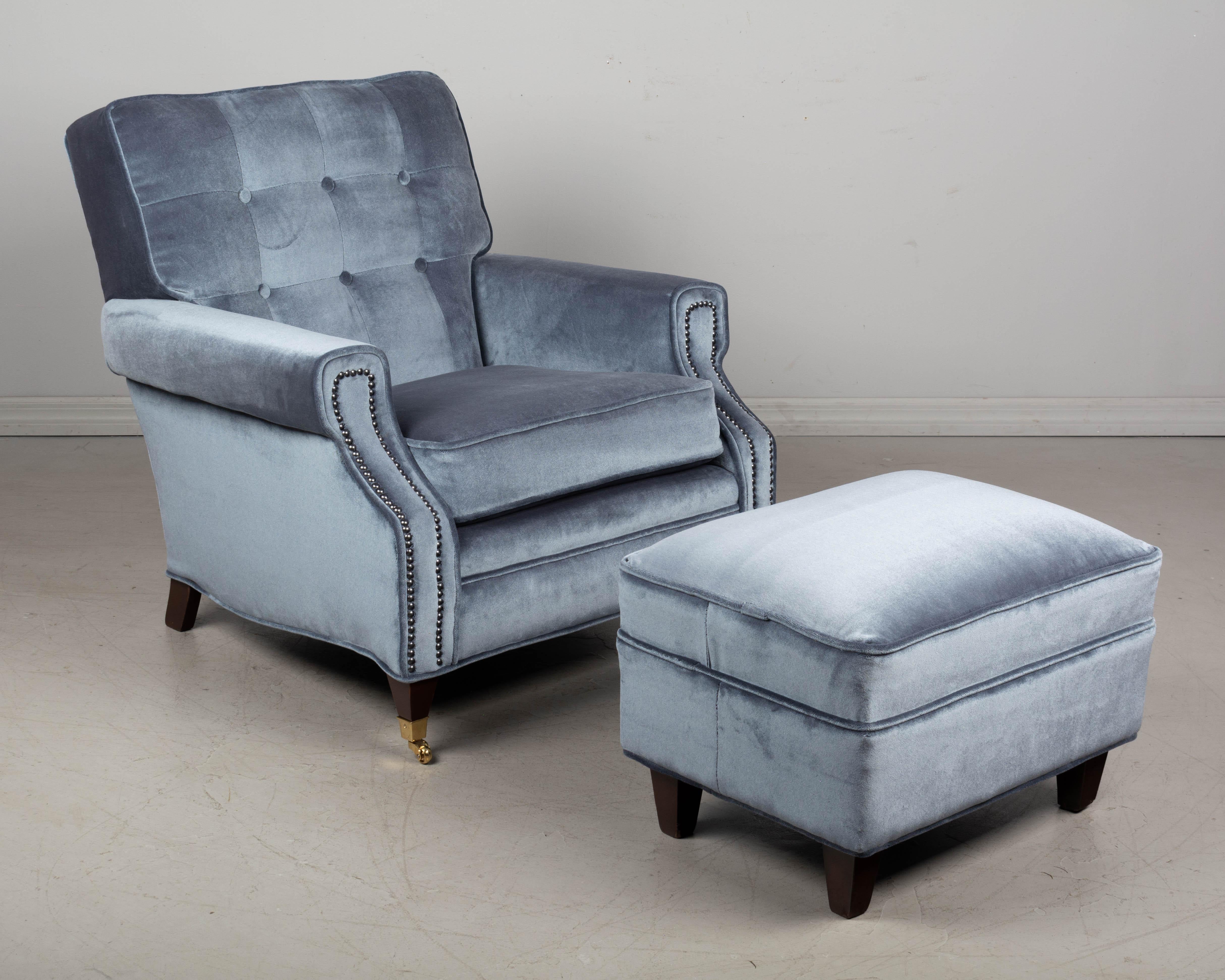A Mid Century Modern club chair and ottoman upholstered in Sunbrella slate velvet. A comfortable lounge or library chair expertly reupholstered in good quality, hard-wearing performance fabric. Tight back with buttons, nailhead trim on arms and new