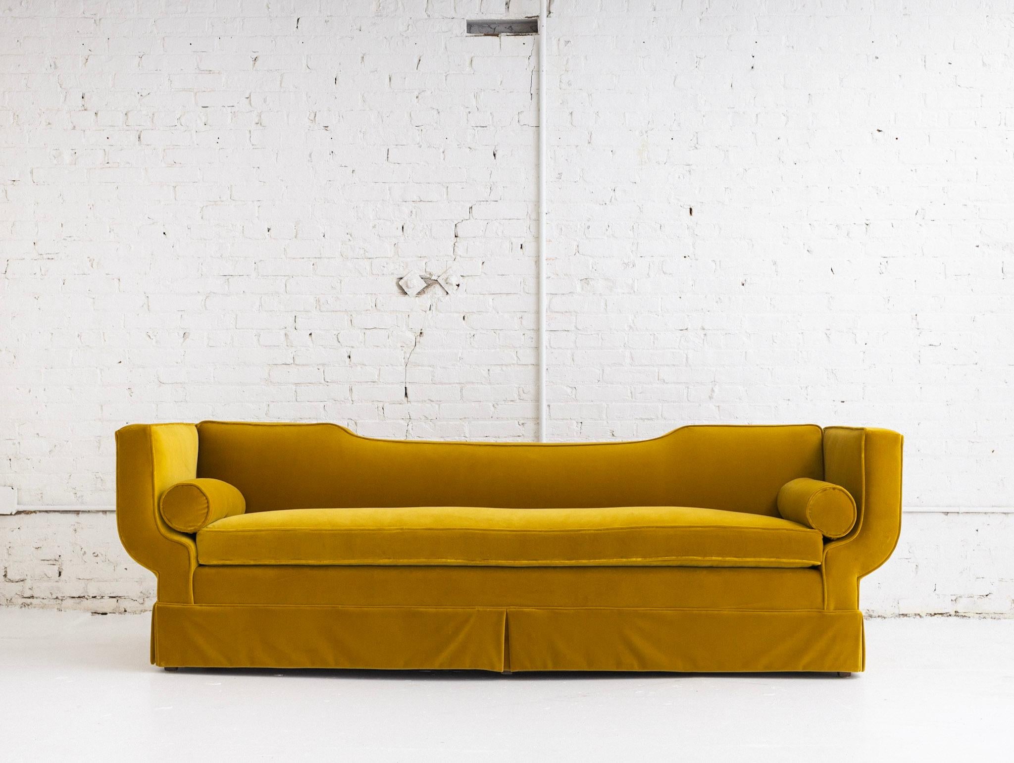 A mid century sofa in the style of James Mont. Newly upholstered in yellow velvet. Gondola silhouette with bolster pillows.