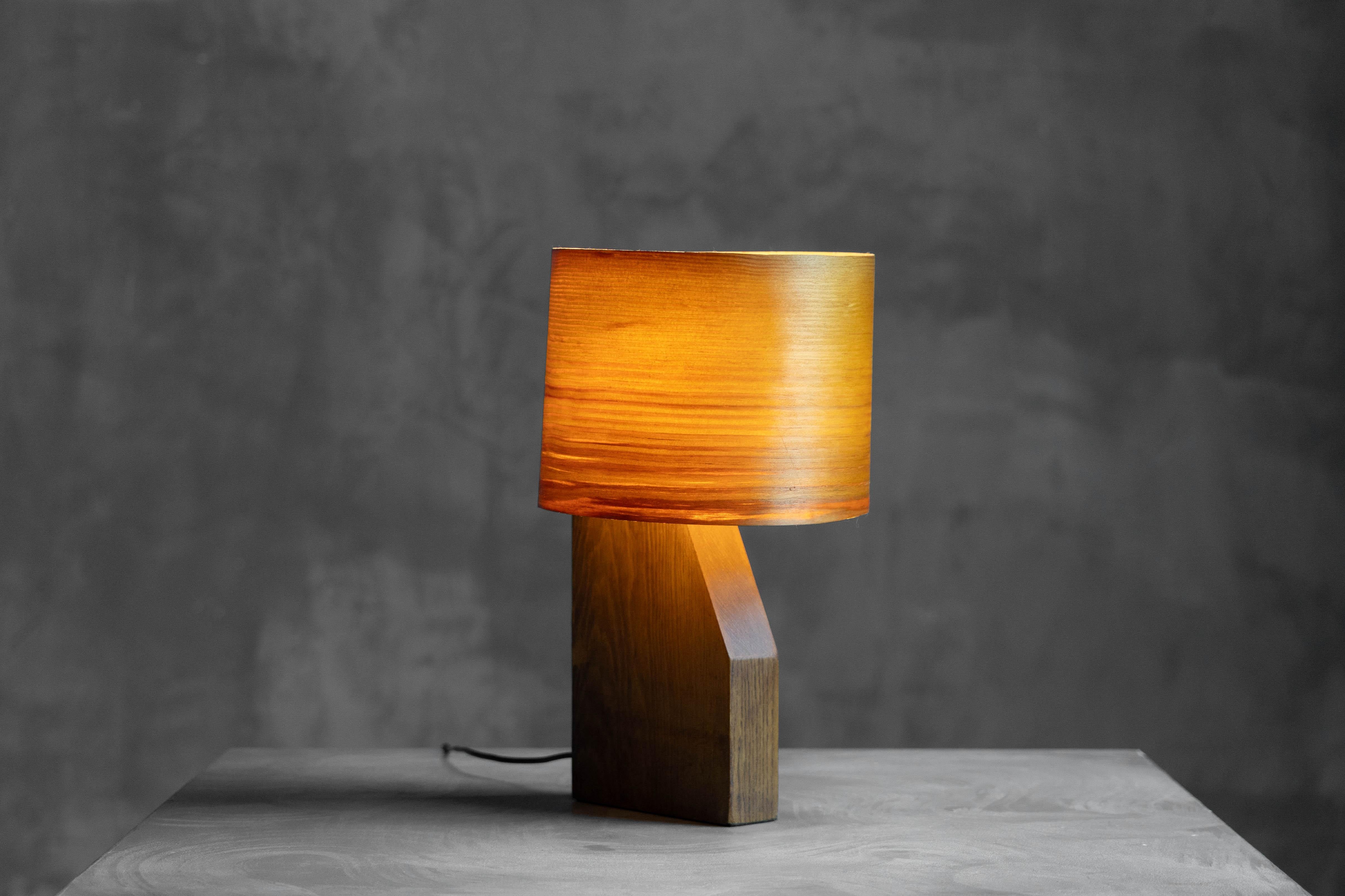 Esta lámpara de chapa de madera de mediados de siglo combina la artesanía orgánica con un estilo moderno atemporal. Su base de madera esculpida y su fina pantalla de chapa de madera crean una luz ambiental y cálida, ideal para rincones acogedores,