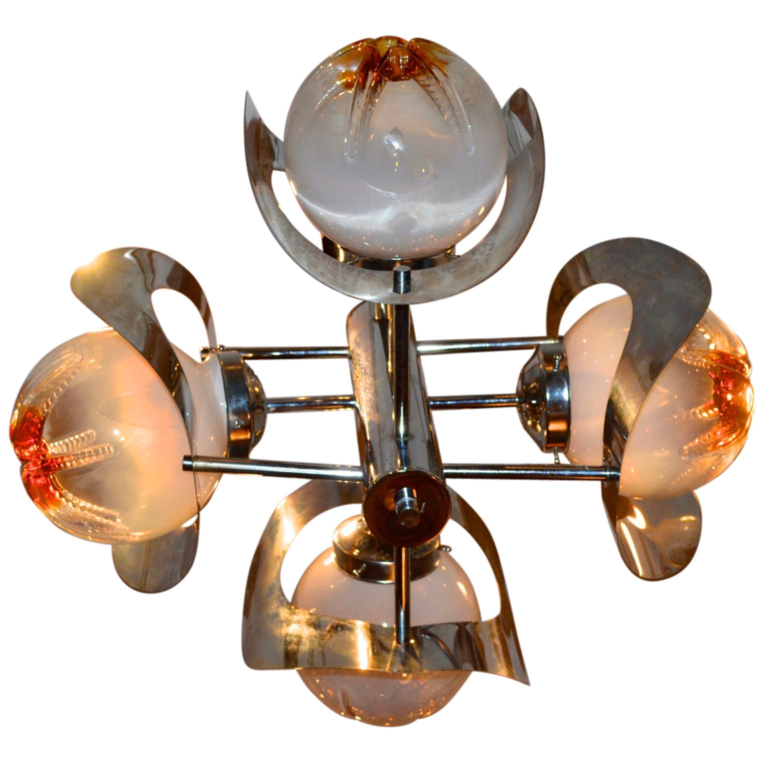 An Italian midcentury Murano art glass four light chandelier designed by Mazzega, chromed metal rod base radiating chrome arms and holding four hand blown mottled frosted amber and smoked glass orbs and curved chrome reflector shades.

   