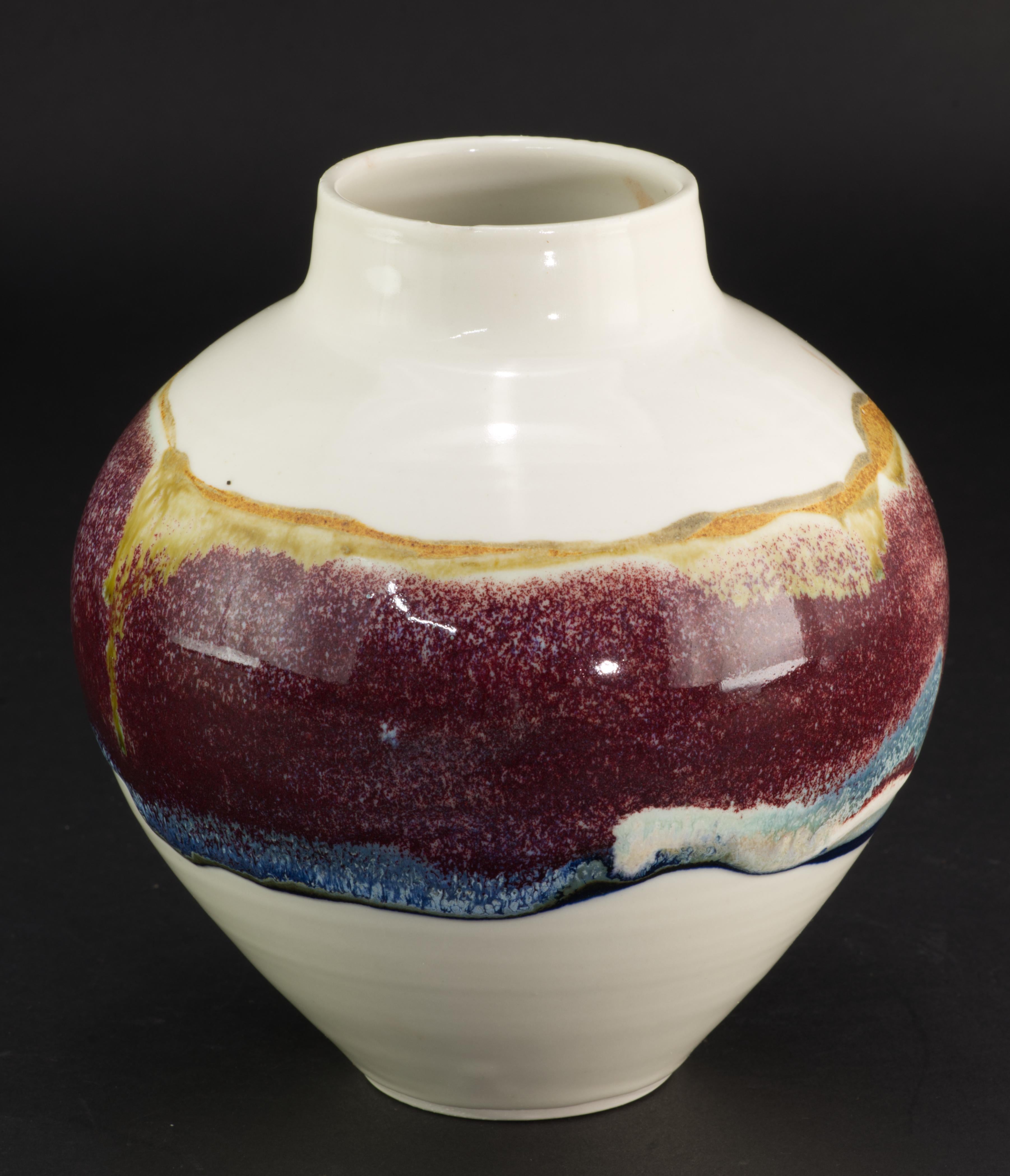  Ce vase en céramique d'art du milieu du siècle a une forme nette et minimale ; il a été réalisé en argile blanche avec une épaisse bande de glaçure de lave grasse multicolore vibrante sur la partie la plus large du corps ; une glaçure blanche