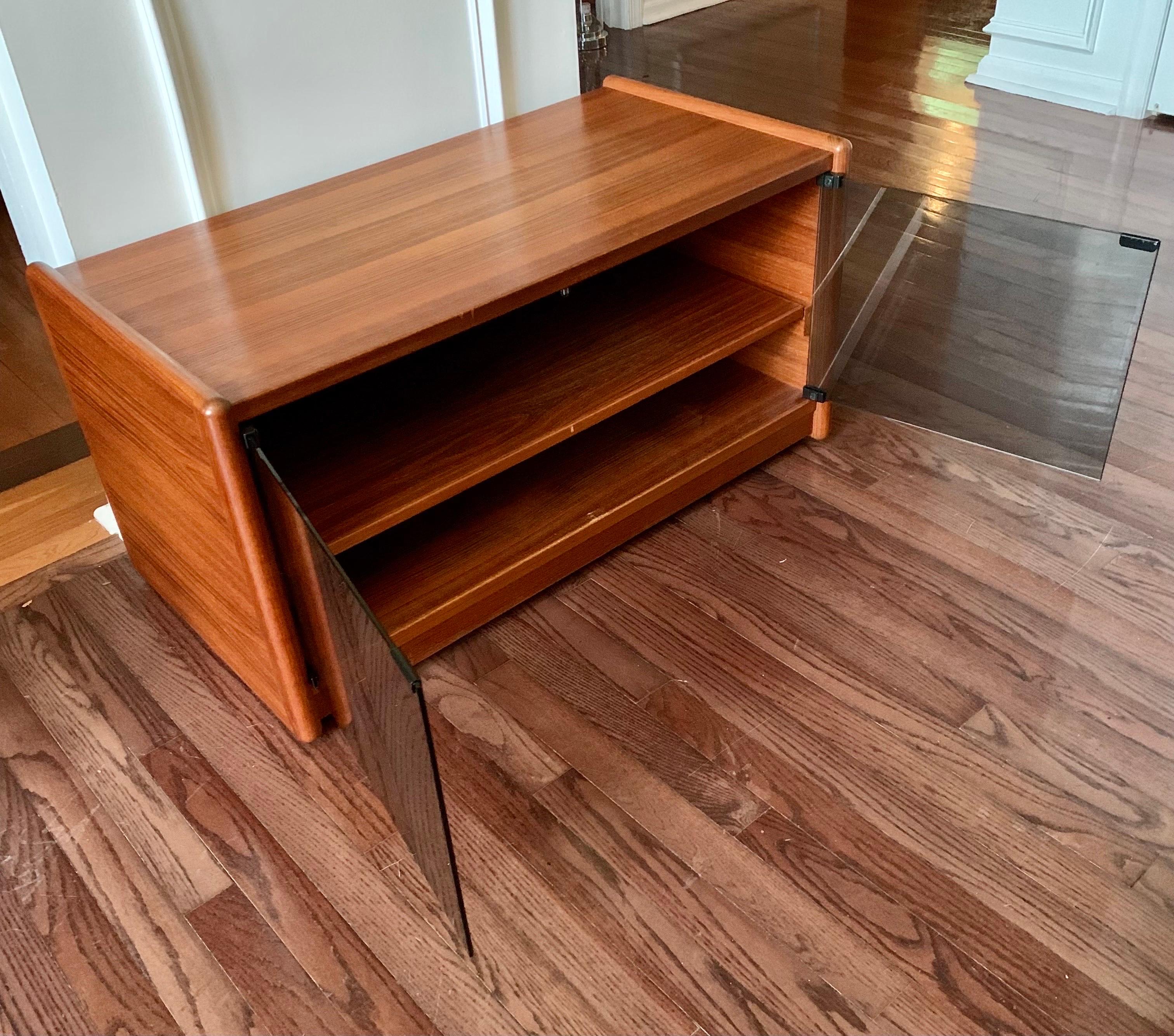 Very clean Vildbjerg Mobelfabrik teak rolling credenza/cabinet with smoked glass. Glass doors close magnetically and cabinetry features an internal pullout shelf. Great for smaller spaces due to its size and maneuverability. Wheels move smoothly. In
