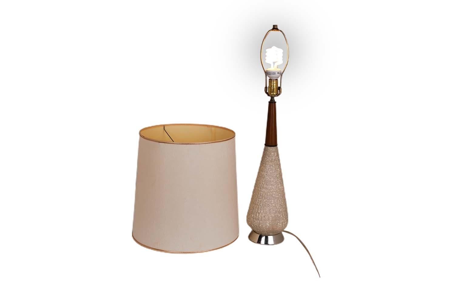 Mid-century modern atomic plaster and walnut table lamp with original shade, circa 1960s. Features a teardrop-form textured bisque base with ivory flecks with a tall walnut neck above a gold-tone metal base. The original tall drum shade has gold
