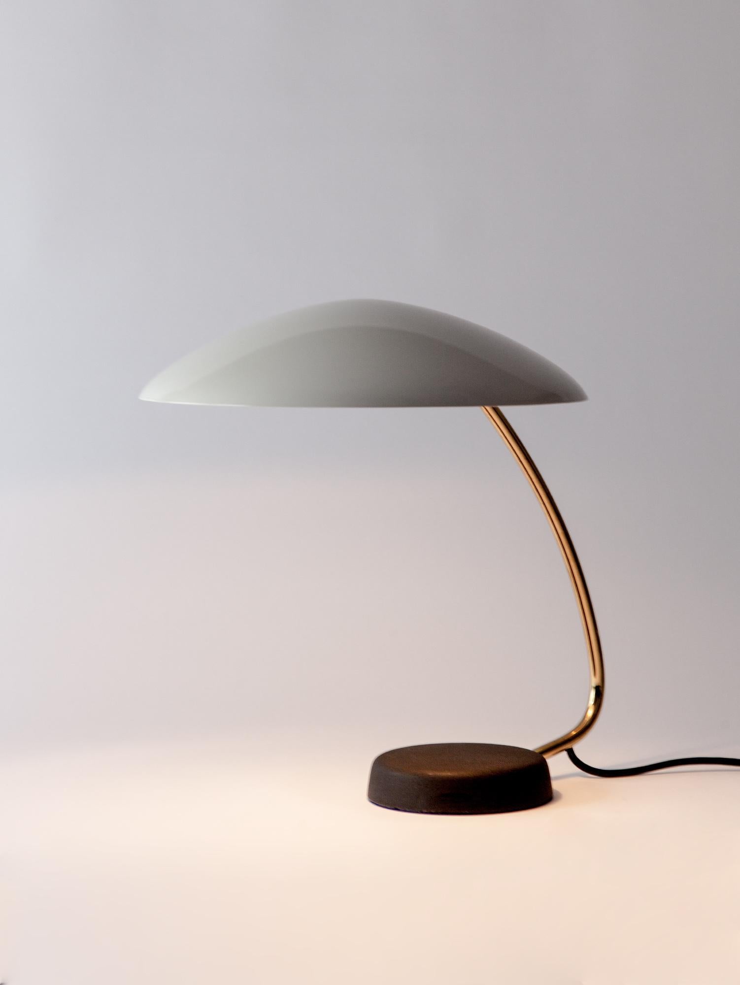 Stunning vintage table lamp by Cosack Leuchten. Sitting on a solid black base, with its original textural paint, the rounded form is continued in the white shade. The curved brass stem detail allows the shade to tilt. Made in Germany in the