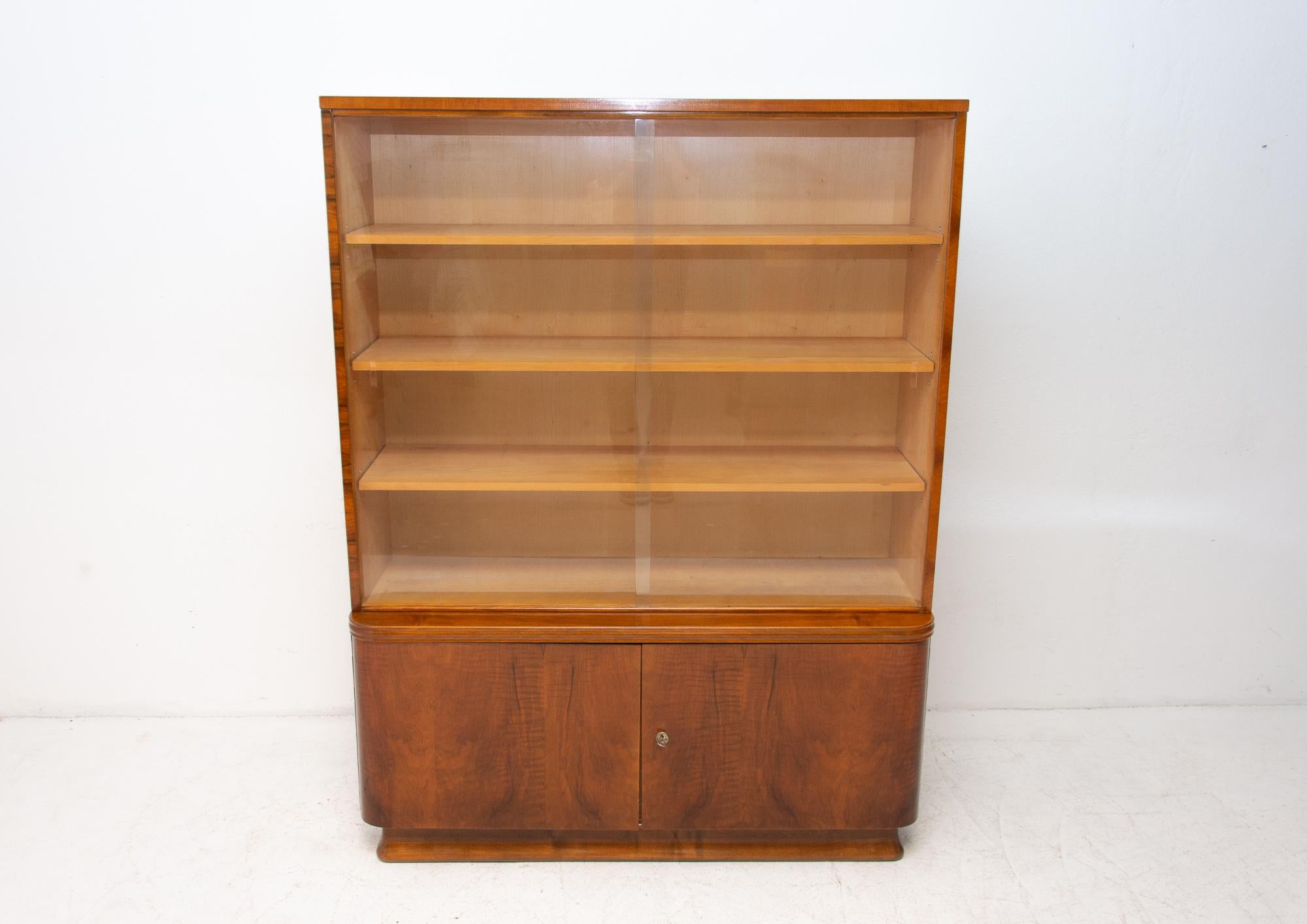 Midcentury vintage bookcase from the 1960s. It was made in the former Czechoslovakia. Features a simple design, a glazed section with four storage spaces and two lockable at the bottom. In Very good condition. Beautiful walnut veneer, plywood.