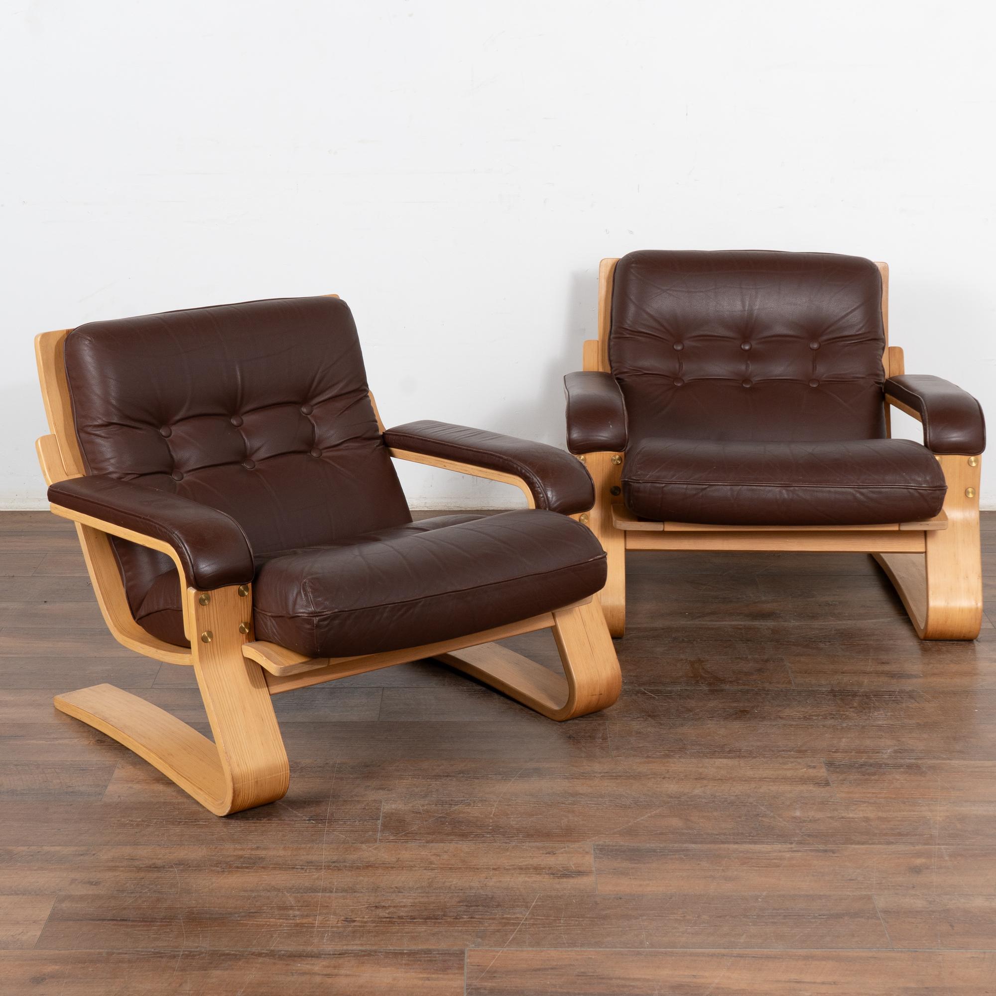 This pair of armchairs shows off the clean lines of mid-century craftsmanship and style. 
In good used condition with the original brown leather showing typical signs of age-related wear such as scuffs, scratches, impressions to leather and minor
