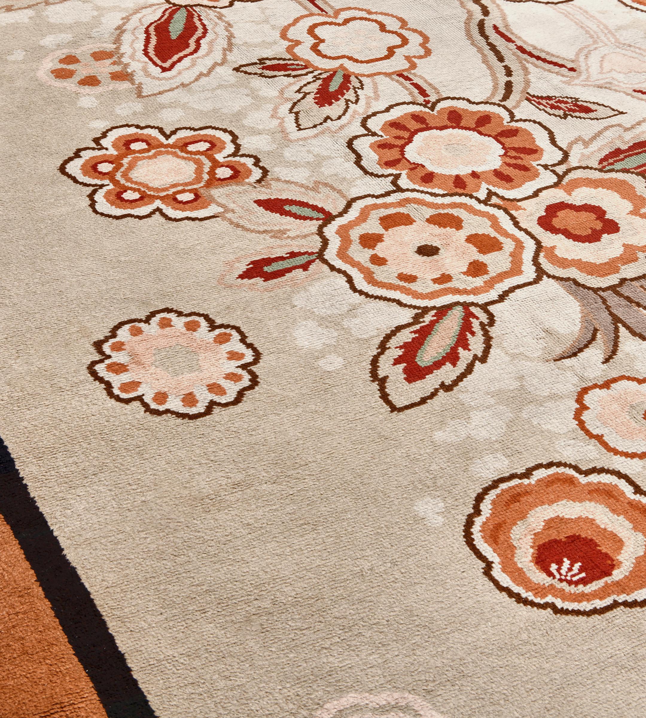 Ce tapis européen d'époque, vers 1940, présente un doux champ brun chamois avec un audacieux capitule de fleurs orange terracotta, brun taupe et ivoire et une vigne feuillue reliée par une large tige, divers capitules de couleur similaire de chaque