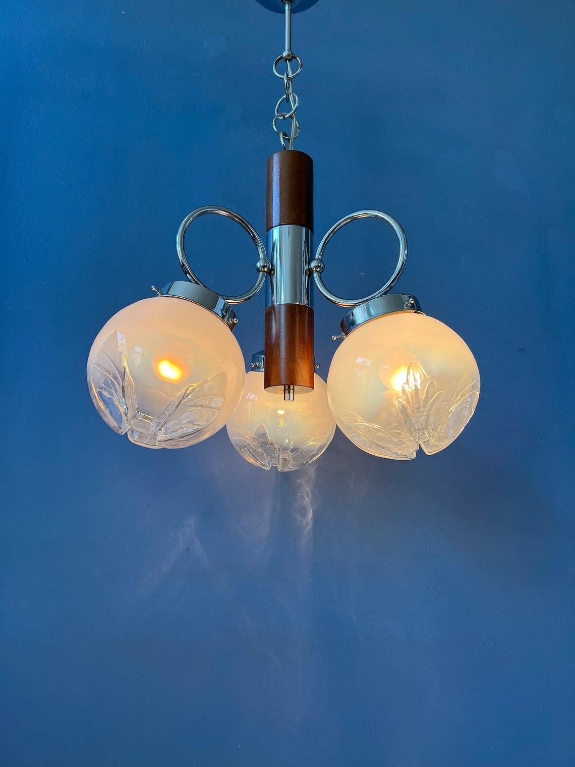 A classic murano chandelier by or in style of Mazzega. The lamps has three glass made shades and has a chrome frame with a wooden element. The lamp requires three E14 lightbulbs.

Additional information:
Materials: Glass, Metal 
Period: