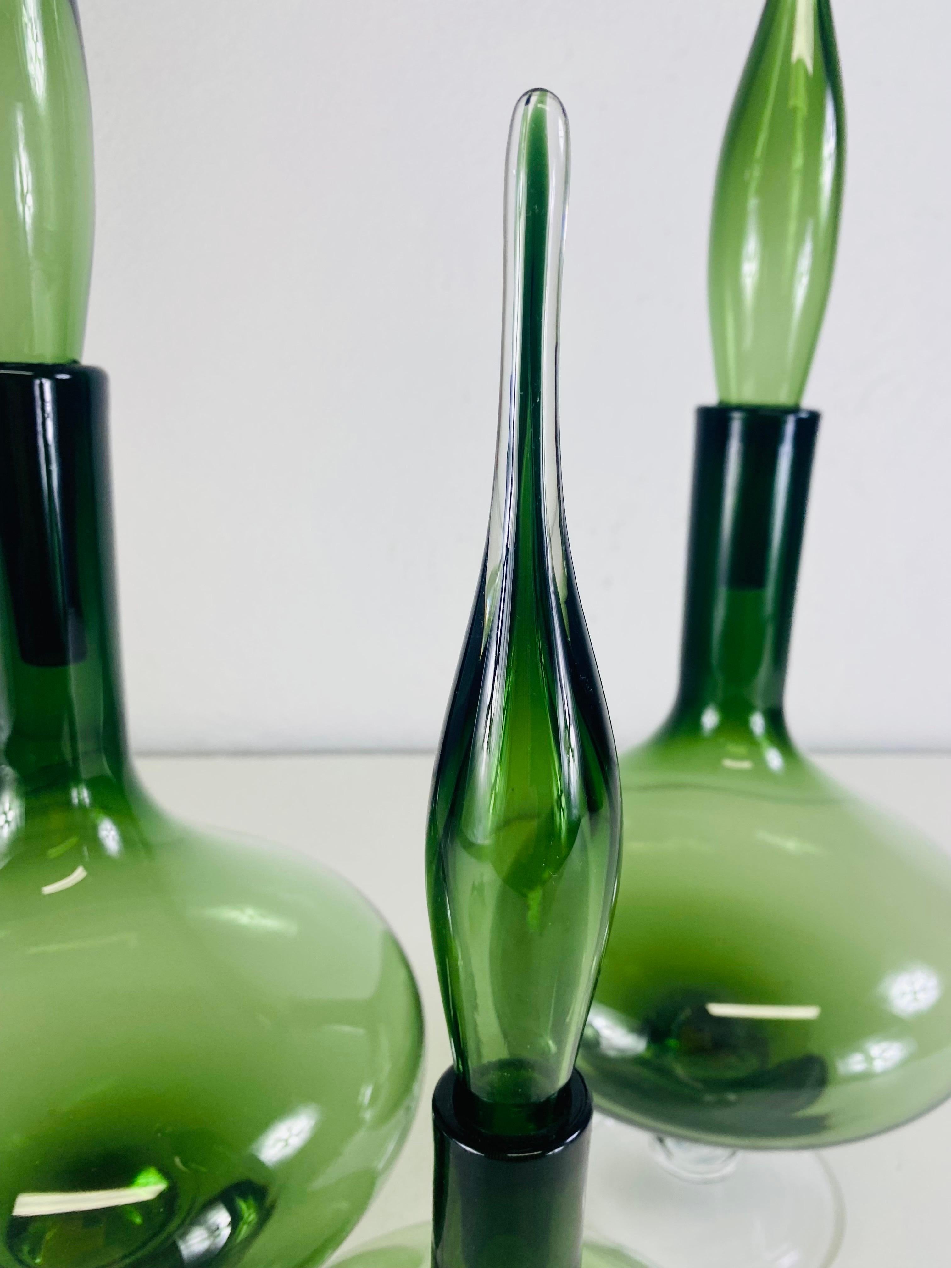 Se trata de un conjunto complementario de tarros de cristal artísticos modernos vintage de mediados de siglo con sus tapones originales. Estos tarros están soplados a mano con vidrio verde oliva incrustado en vidrio transparente. Este juego de