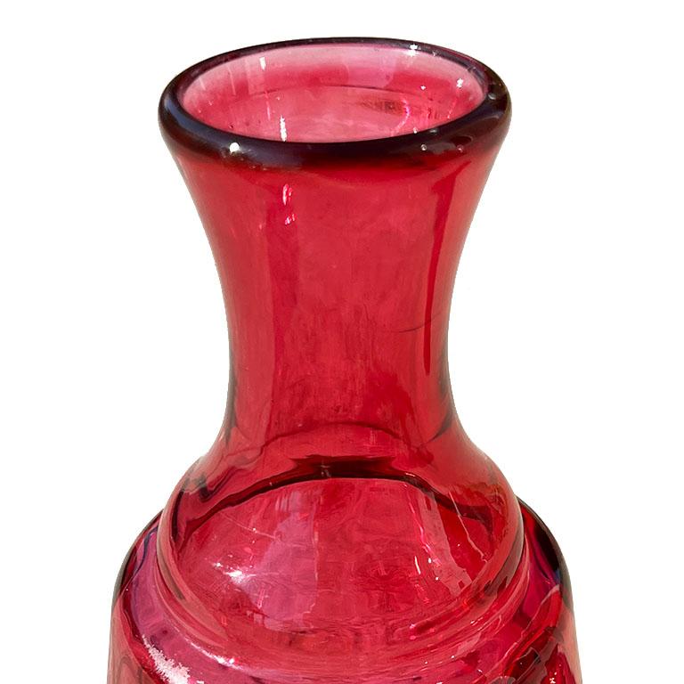 A beautiful early 20th-century cranberry glass decanter, carafe, or vase. With a wide bottom and narrow neck, this piece could be used in any number of ways. While we do not know the brand, it does seem to mimic the style of some Fenton pieces we