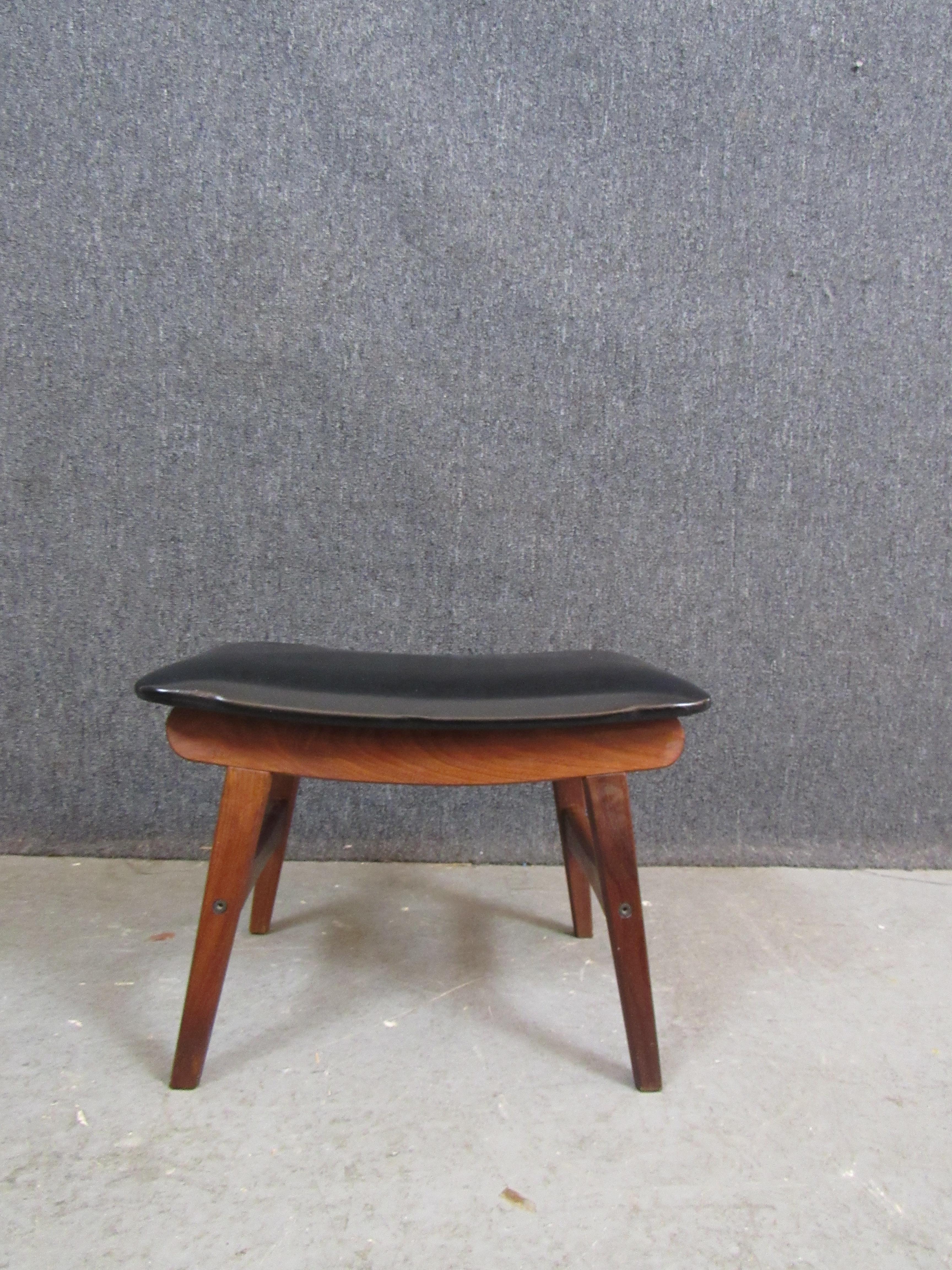 Put up your feet and enjoy all the comfort and charms of mid-century Danish design with this wonderful teak ottoman made by Fredly Möbelfabrik of Denmark. With warm wood grain, a pagoda-inspired silhouette, and a sleek black faux leather cushion,