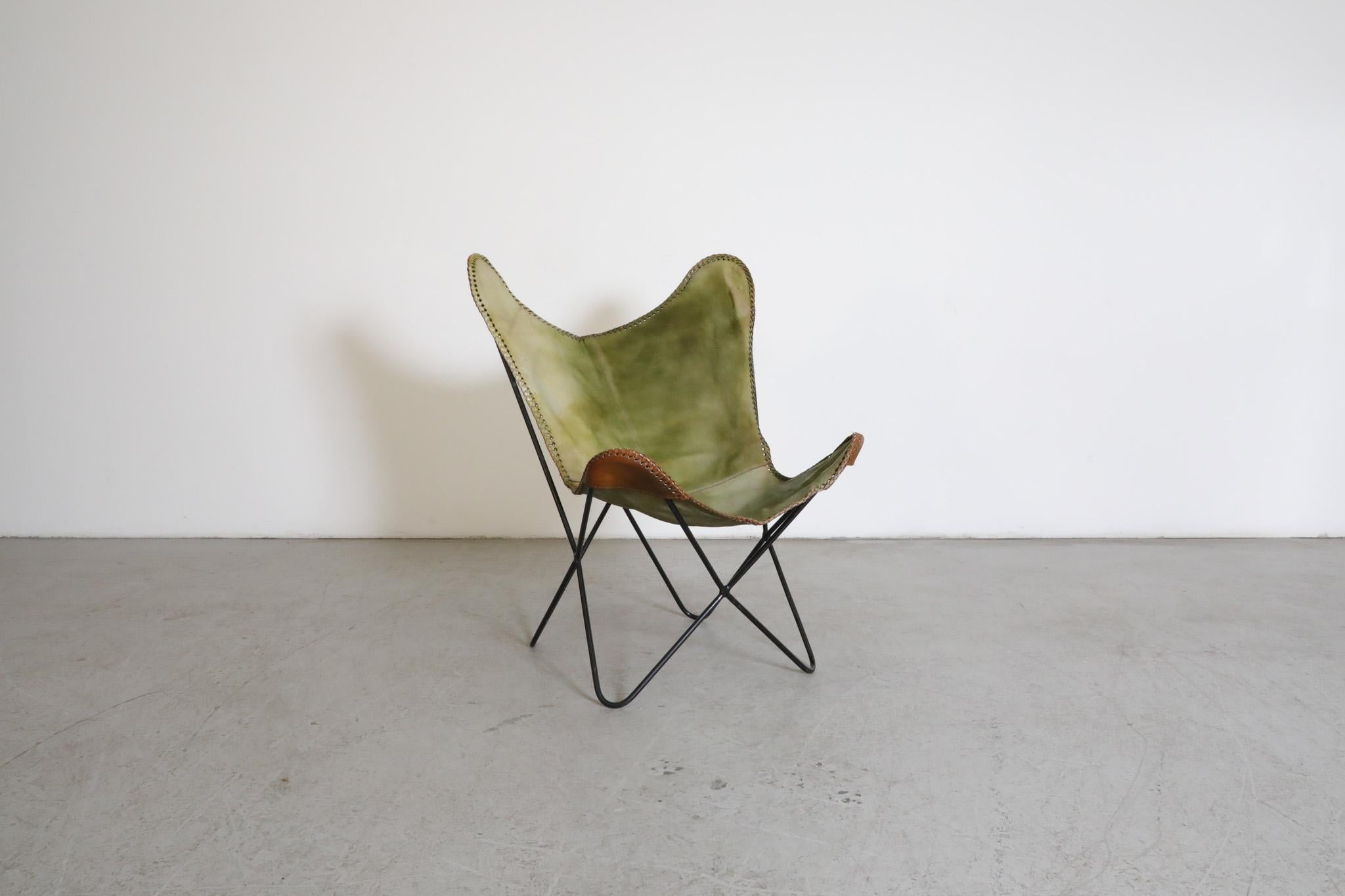 Mid-Century Jorge Ferrari-Hardoy attributed butterfly lounge chair with black enameled metal wire frame. The sling seat is crafted in faux green and brown leather an with woven edging. A comfortable and lightweight lounge with hand stitching and