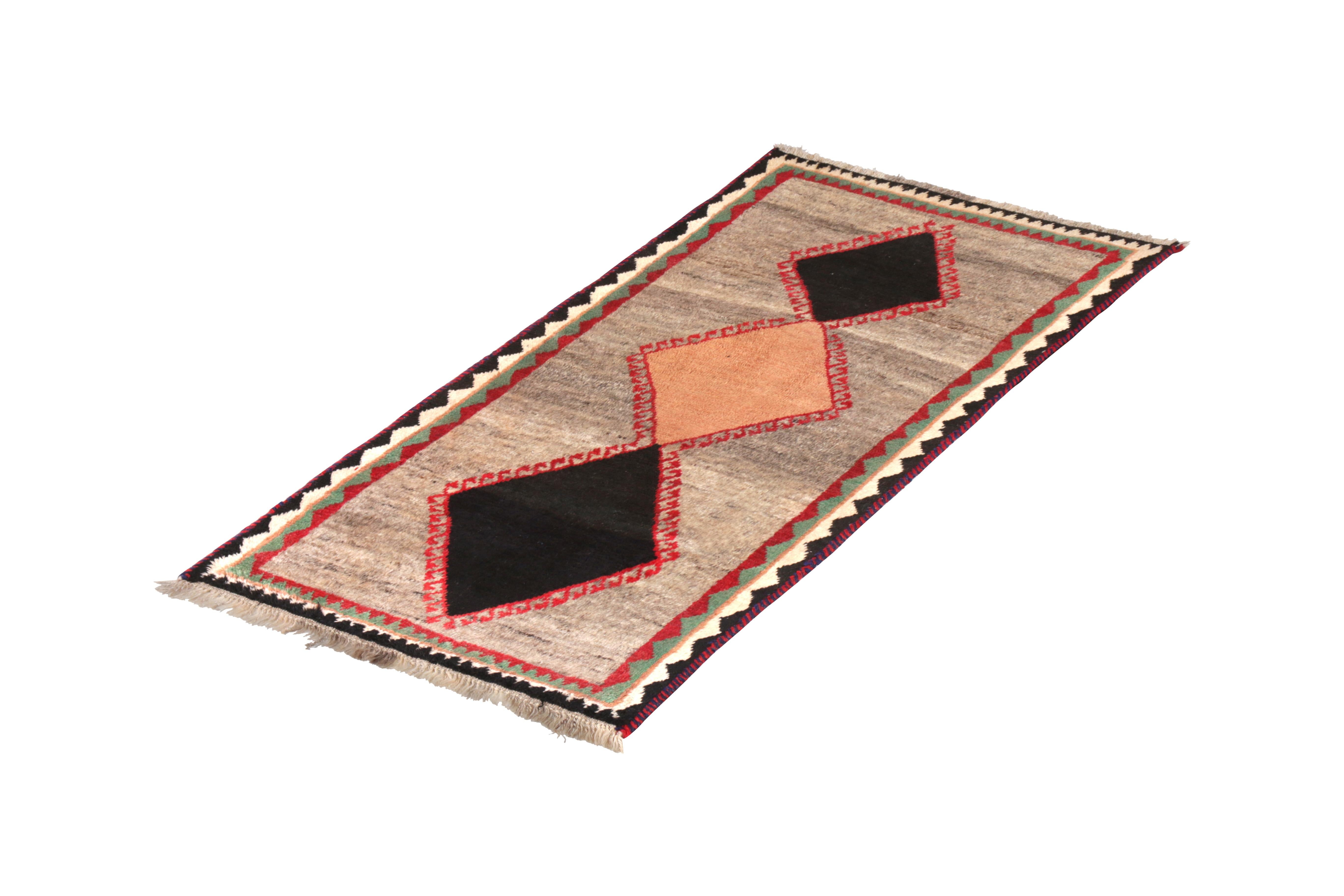 Hand knotted in wool pile originating circa 1950-1960, this vintage Persian runner connotes a mid-century tribal Gabbeh rug design in a lively transitional colorway, playing black, beige-brown, and other tribal hues against a silver-gray field
