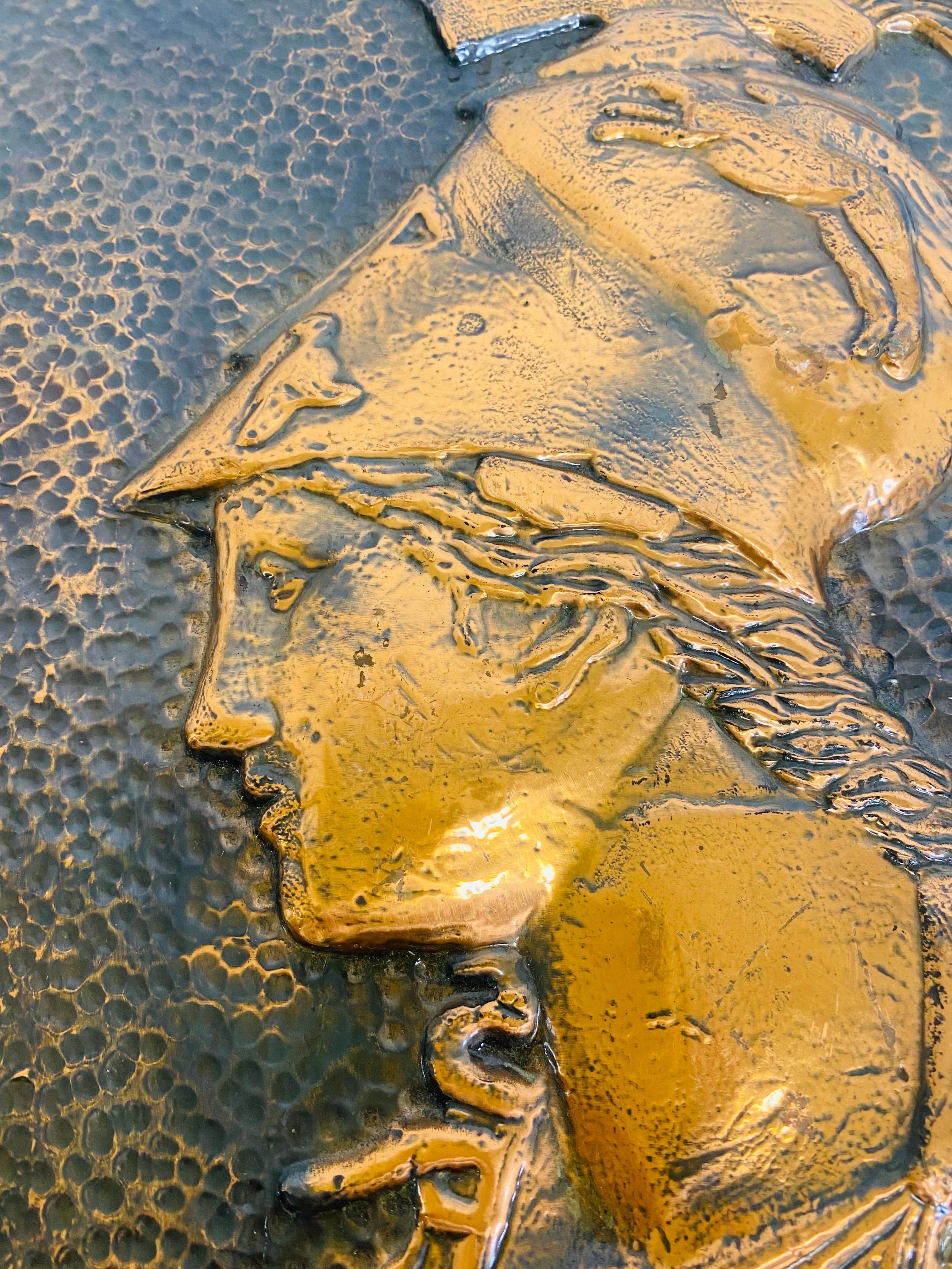 This is a mid-century vintage hand hammered Greco-Roman wall plaque. This copper plaque has an appropriate patina to the surface of the copper for its age and history. This plaque is a side view of a Greco-Roman soldier with an elaborate ornamental