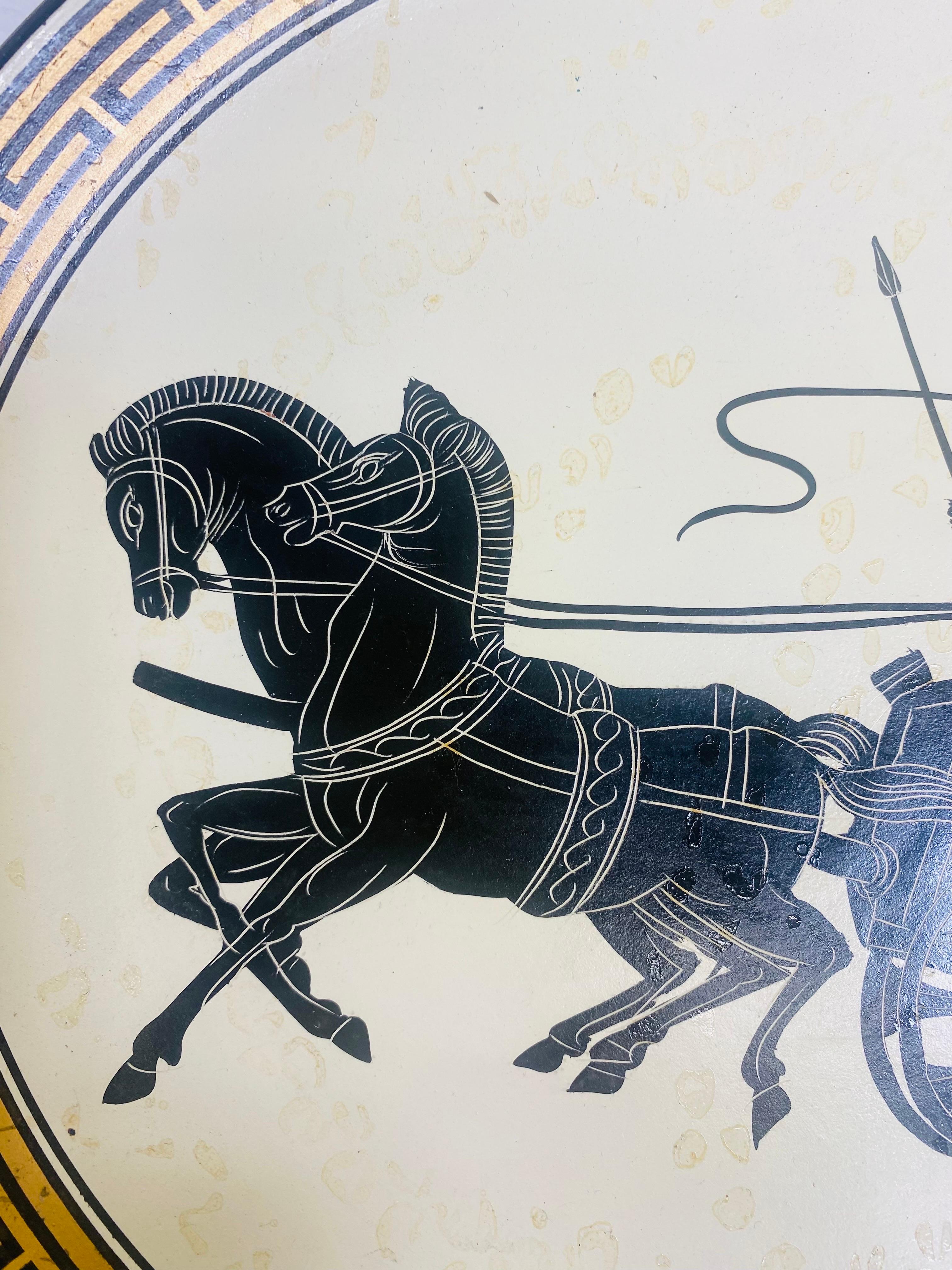 This is a mid century hand-painted terra-cotta charger. This hand-painted plate has a Greek key decoration around the edge with a warrior on a chariot in the center. This plate has the artist name and handmade in Greece on the reverse. This plate