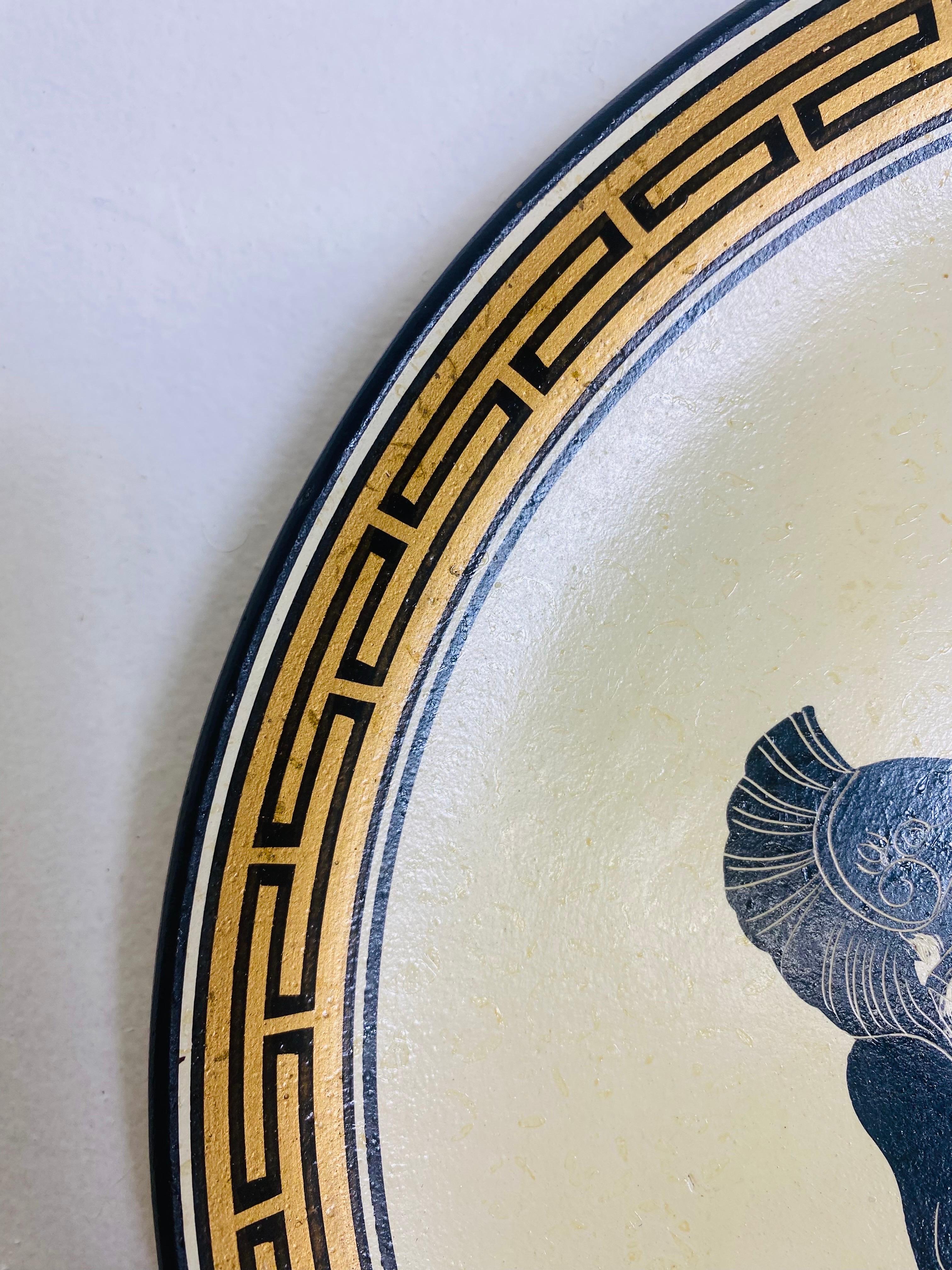 This is a mid century handpainted terra-cotta charger. This hand painted plate has a Greek key decoration around the edge and a pair of Warriors in the center. This plate has the artist name and handmade in Greece on the reverse. The Plate has a