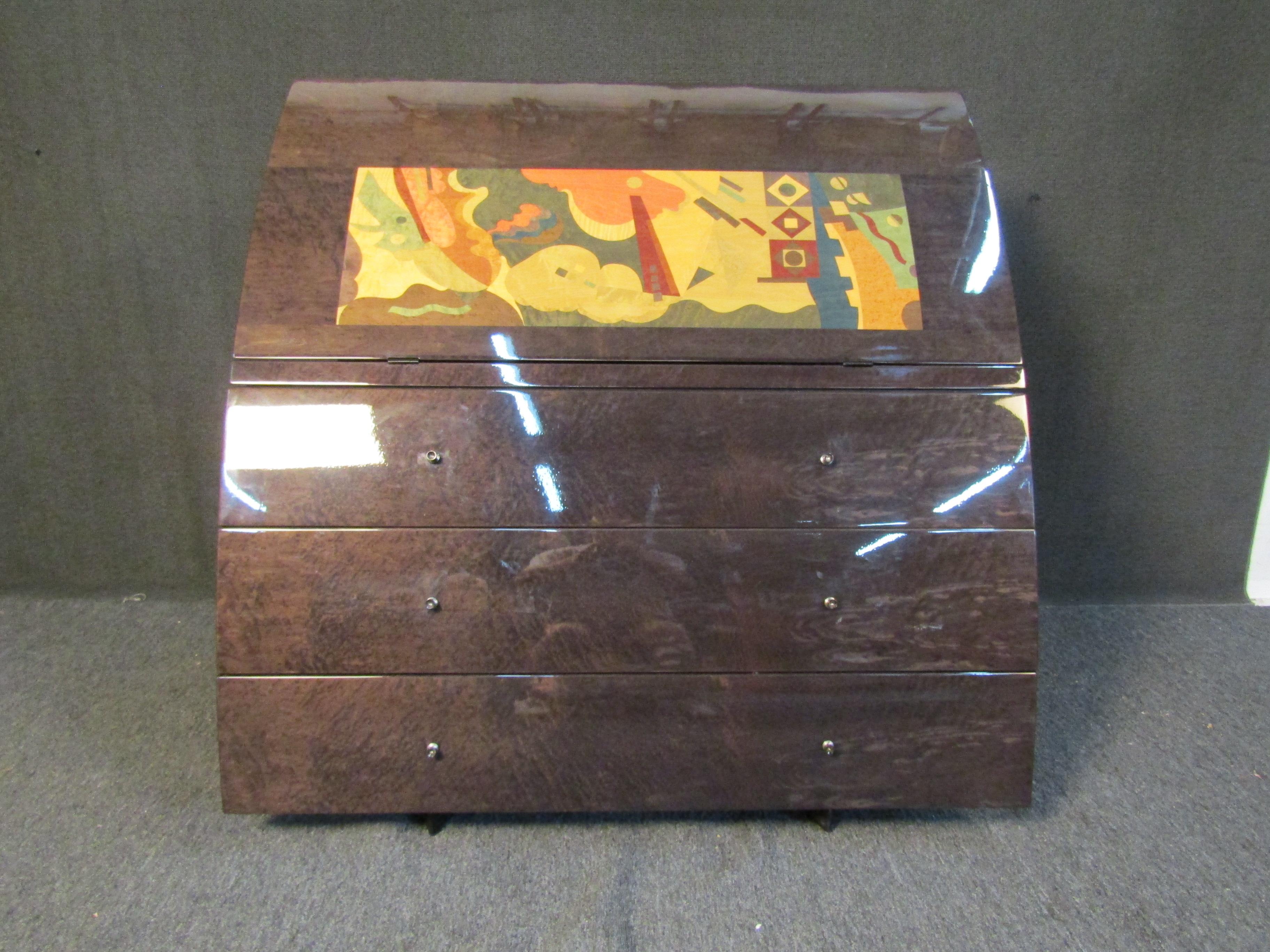Scrivania vintage in stile metà secolo con intarsio astratto colorato sul davanti. La parte anteriore ribaltabile rivela un'ampia superficie di scrittura, oltre a ripiani e cassetti per l'organizzazione. Tre ampi cassetti sottostanti offrono ampio