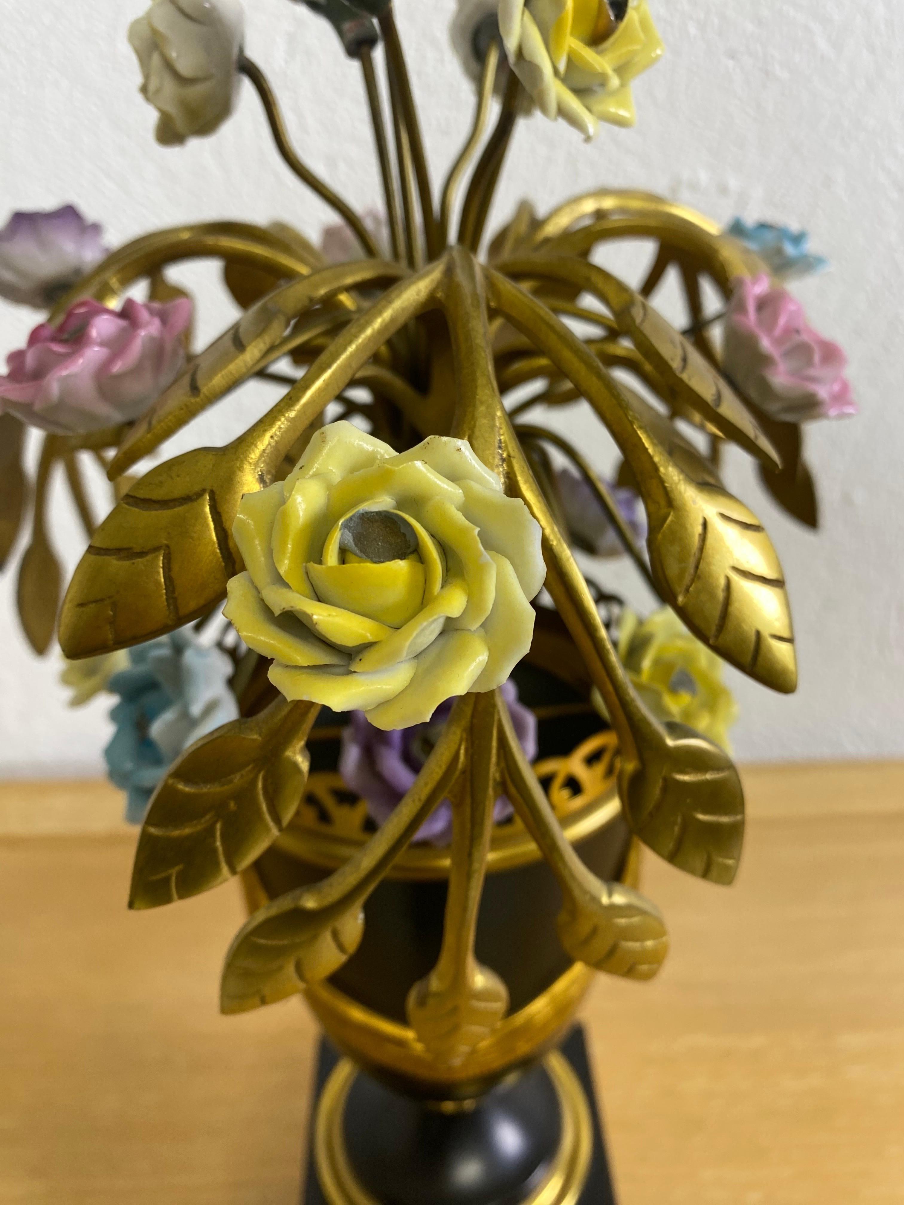 This is a mid-century vintage Italian made decorator table lamp. The table lamp features a botanical inspired bouquet flowers with handmade porcelain flowers nestled in brass leaf design. The base and urn are in black with an empire design featuring