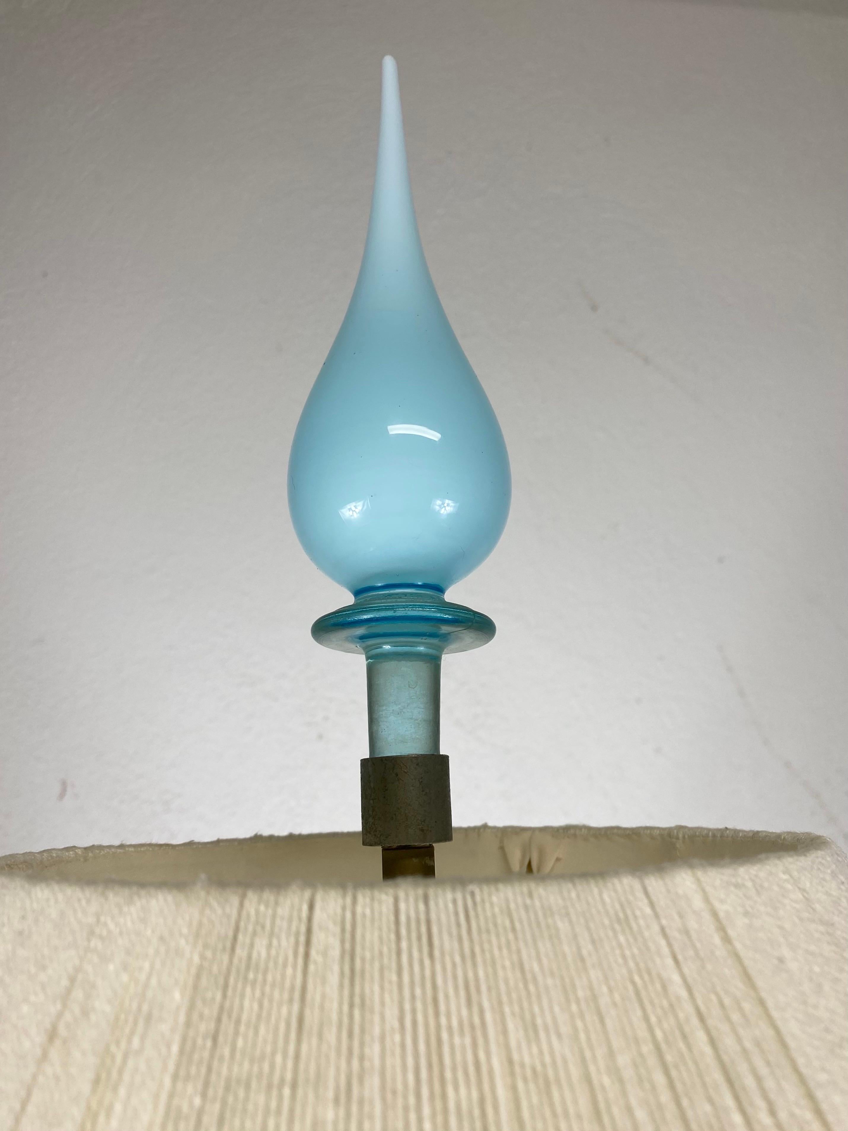 Il s'agit d'une lampe de table en verre opaque bleu de Murano datant du milieu du siècle dernier. Cette lampe est dotée d'un abat-jour de style milieu de siècle, fait à la main et enveloppé d'une ficelle de couleur crème. La lampe a une base en