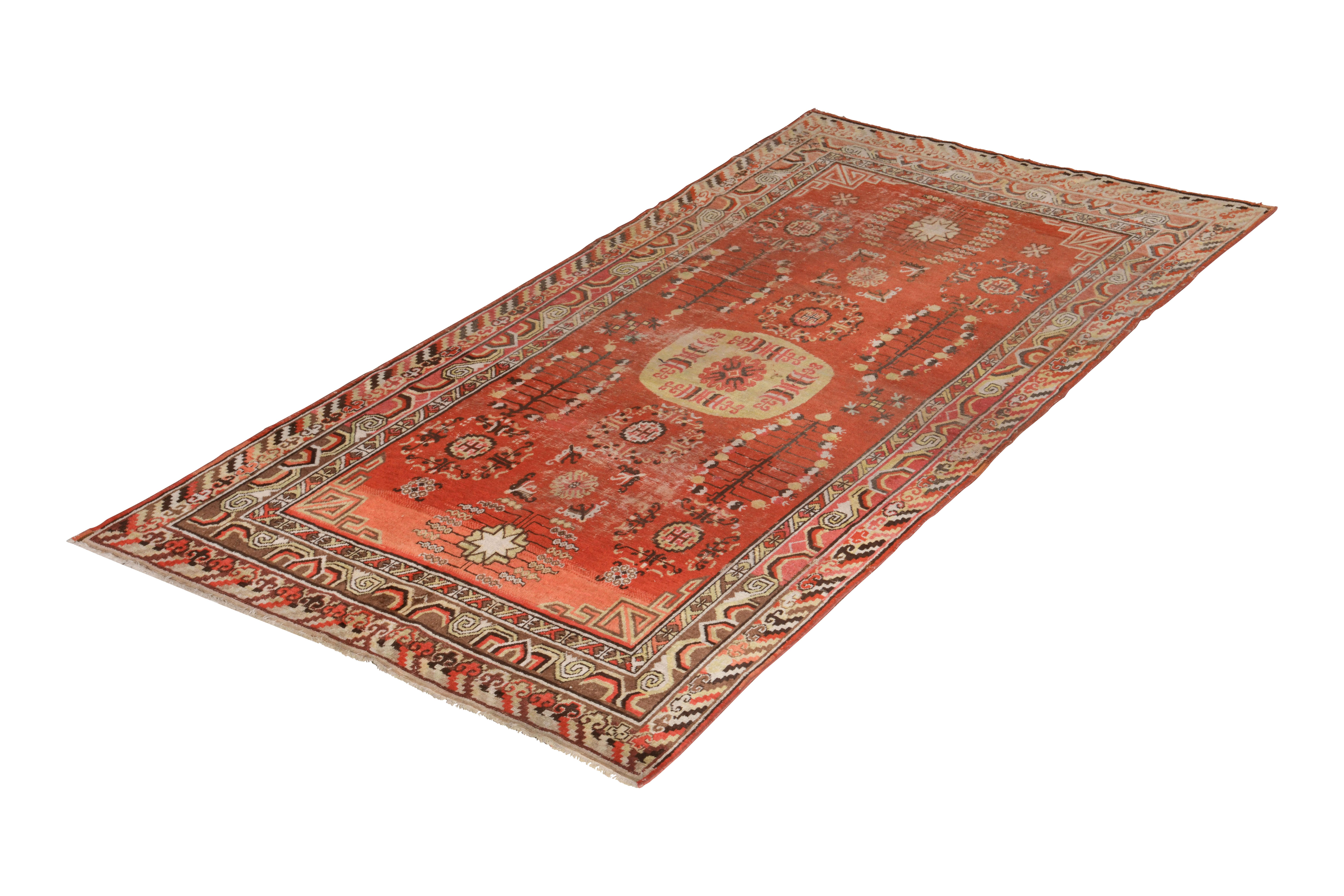 Hand knotted in wool originating from East Turkestan circa 1950-1960, this midcentury piece connotes a vintage Khotan rug design with notable emphasis on regal Chinese medallion patterns in a transitional red and beige-brown colorway. Connoisseurs