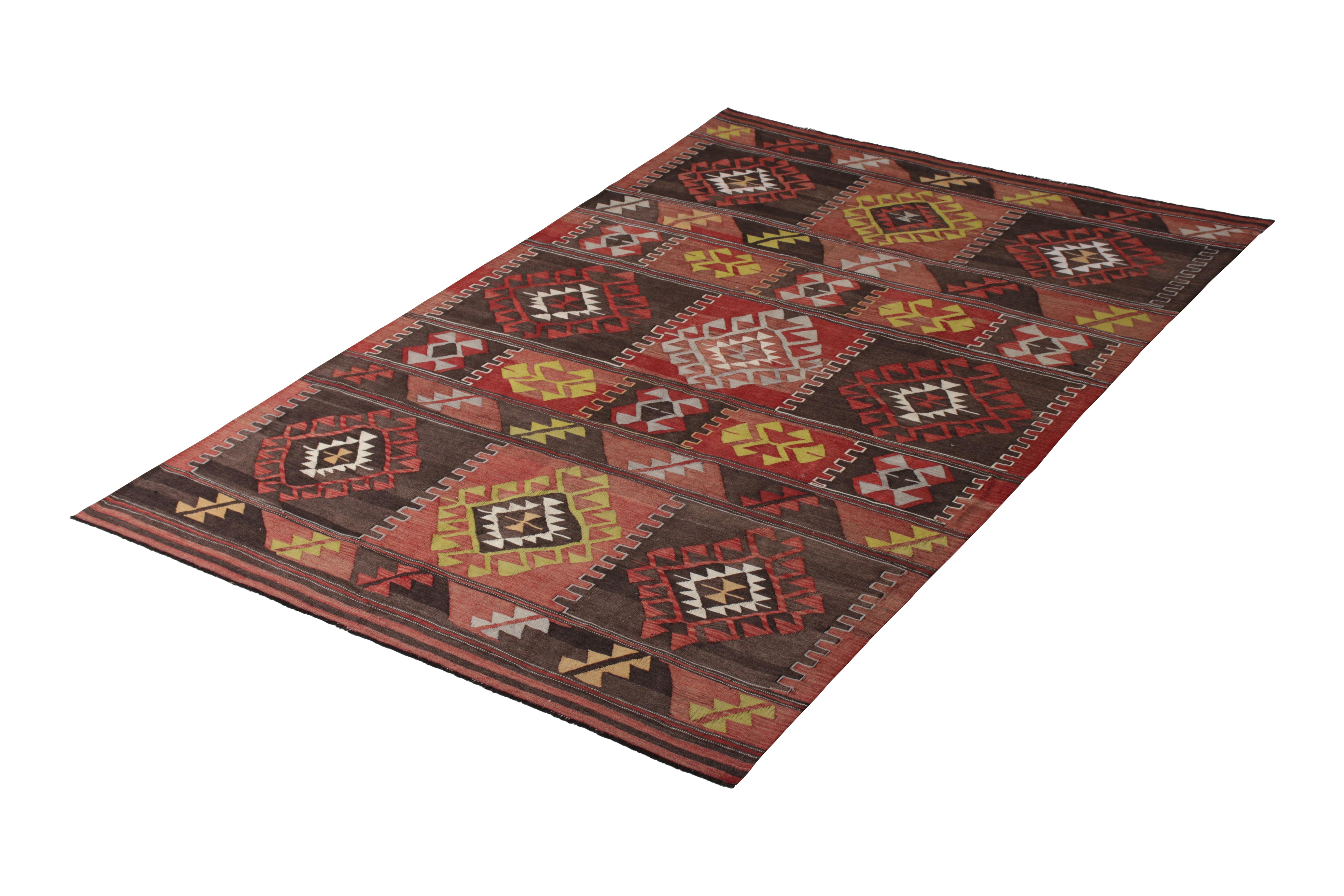 Handwoven in a wool flat weave originating from Turkey circa 1950-1960, this vintage Kilim rug connotes a midcentury tribal design of fabulous color, employing accents of blue and green against a background of red, brown, and pink hues both