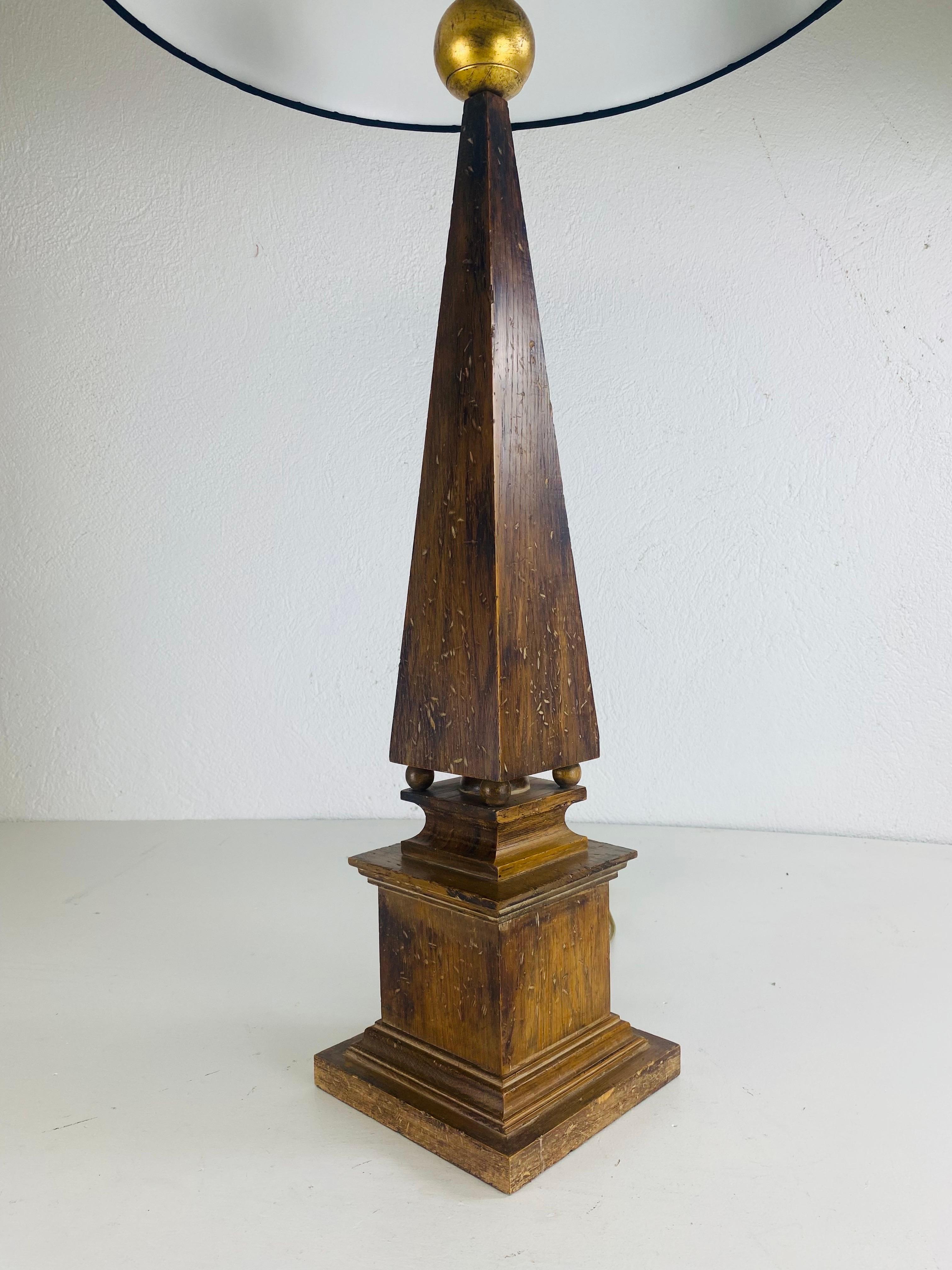 This is a large mid-century vintage walnut obelisk table lamp. This decorator lamp has a black linen shade and comes with his original solid brass finial. This classical obelisk stands on a square plinth with four ball feet and extends upwards to a