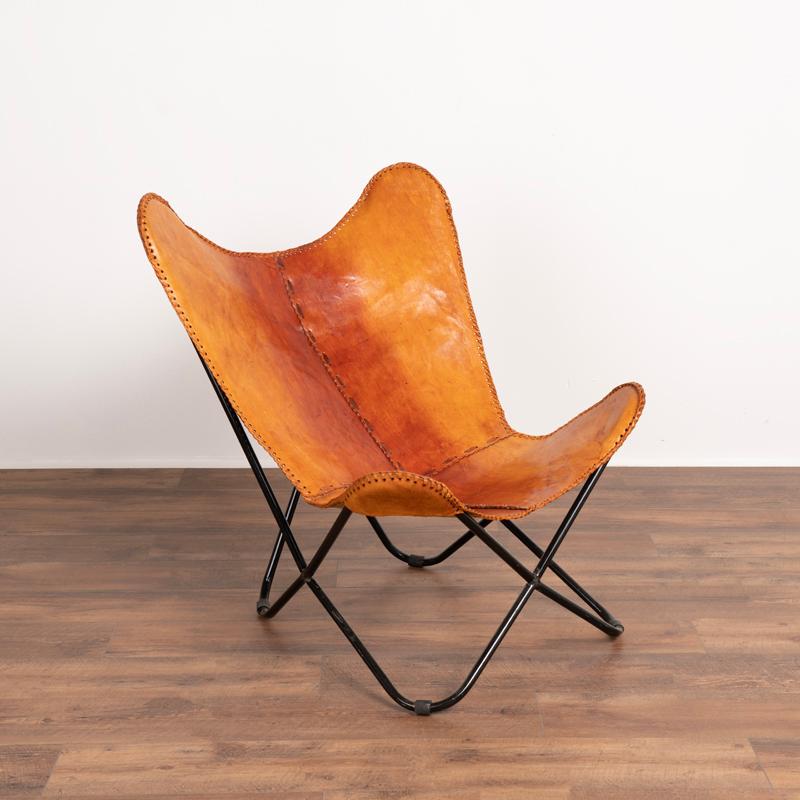 Mid-Century Modern butterfly chair with exceptionally beautiful original leather in cognac on a black base. Note darker patina of leather running down center; age related stains, scuffs, scratches and wear are commensurate with age and do not impact
