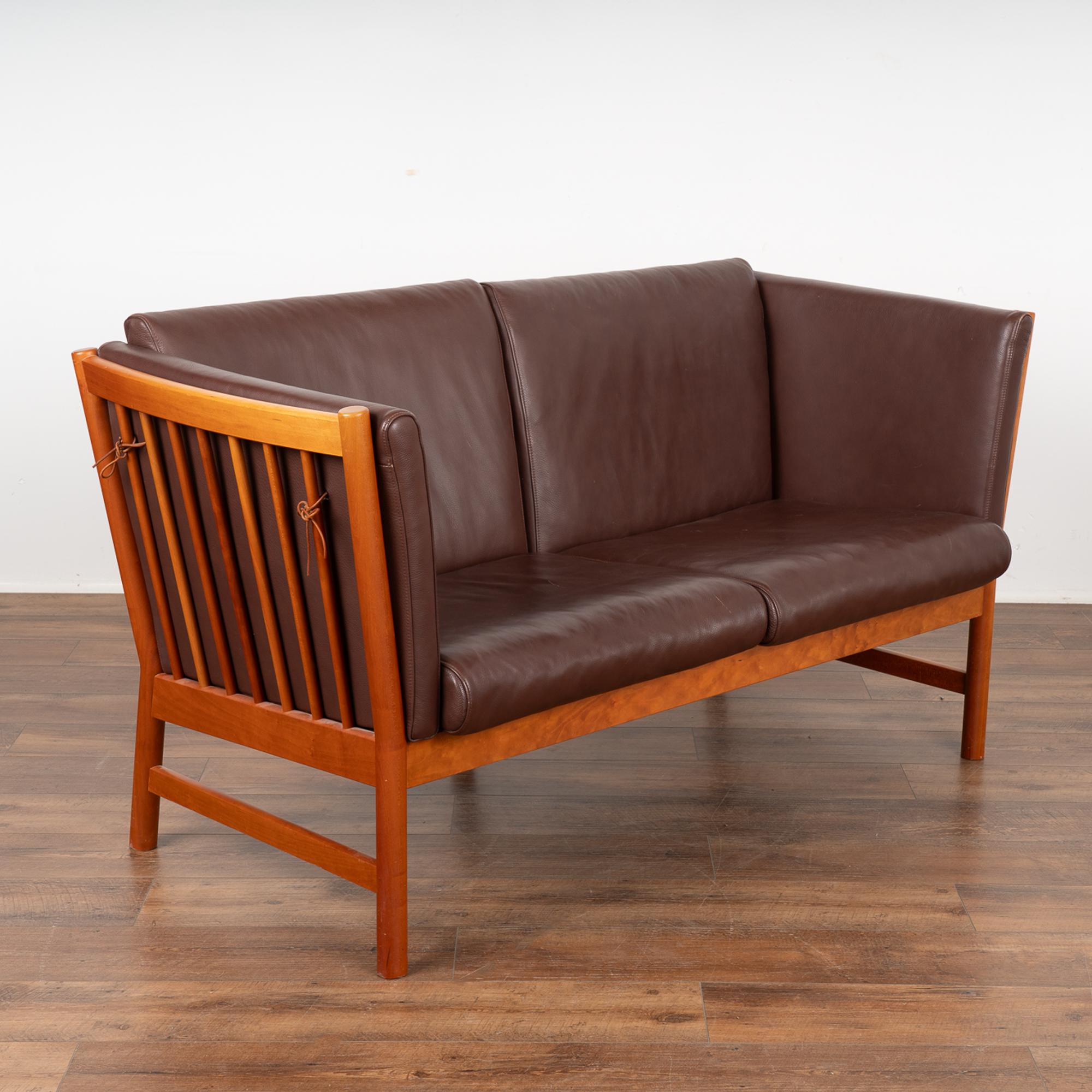 Mid-century modern vintage two seat leather sofa loveseat with spindle sides and back.
This comfortable sofa combining tradition with modern lines; upholstered in burgundy colored leather, loose cushions (side cushions tie to spindle), hardwood legs