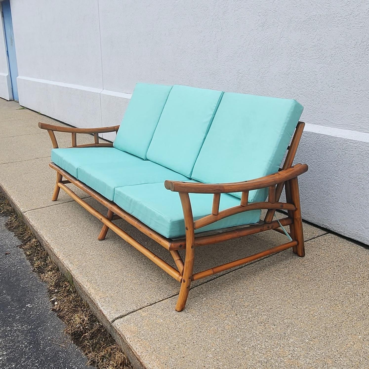 This is a unique Ficks and Reed rattan sofa that comfortably sits 3. Complete with new turquoise blue cushions that has a faint grass cloth pattern. It has an original natural amber brown colored finish with a beautiful sculptural like form. Wire